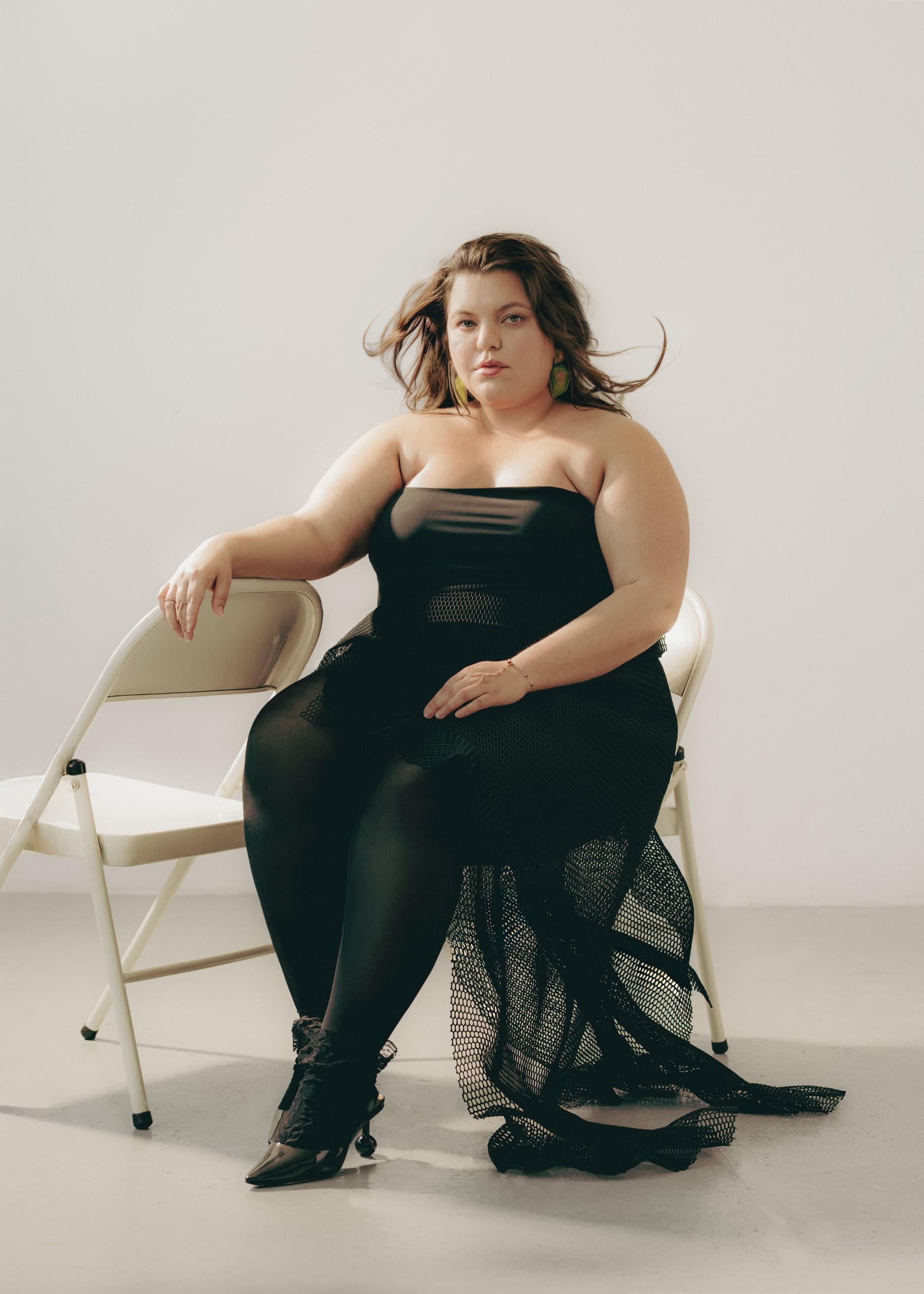 Person in black dress seated on a chair in a minimalist setting.