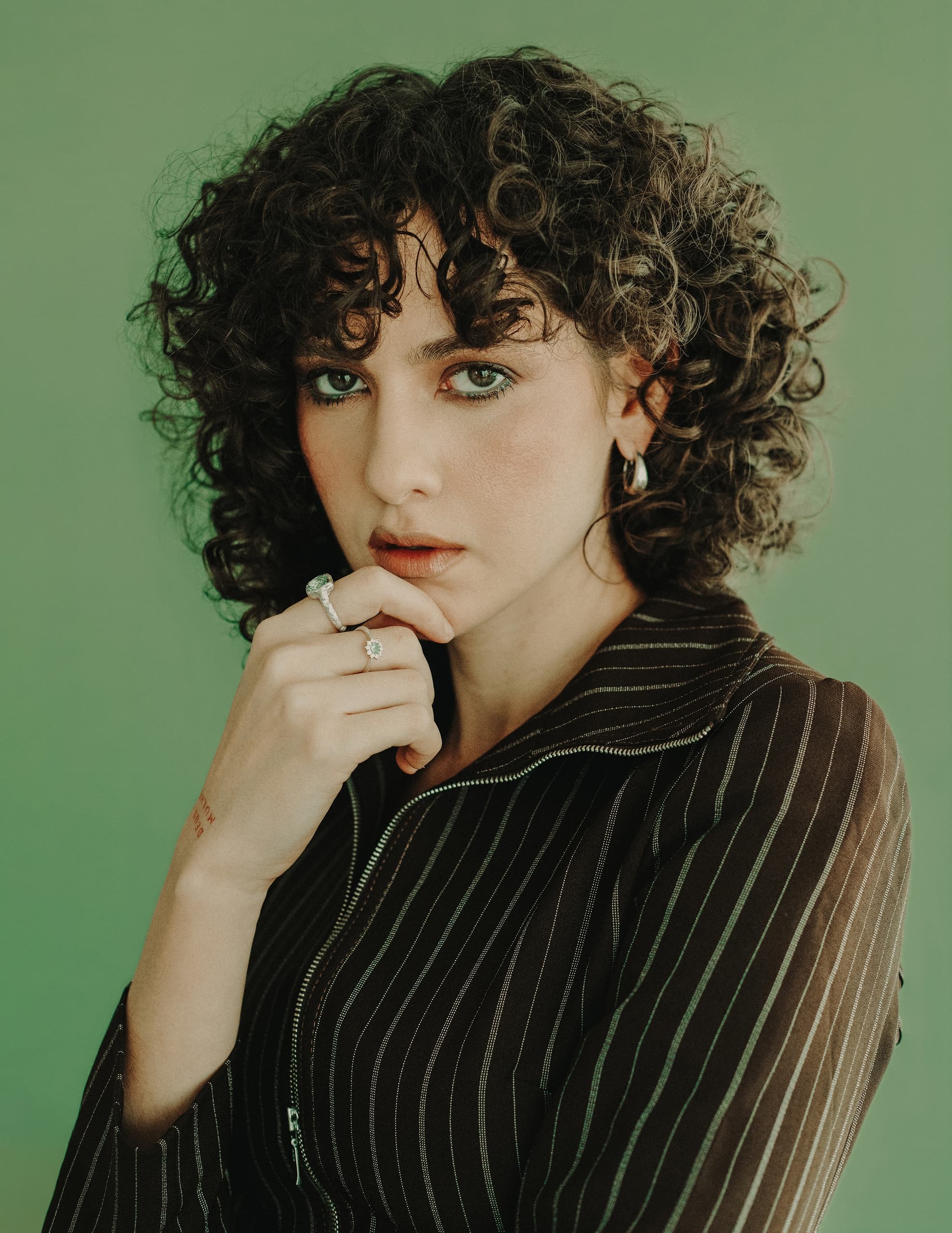 Woman with curly hair posing against a green background in a striped outfit.