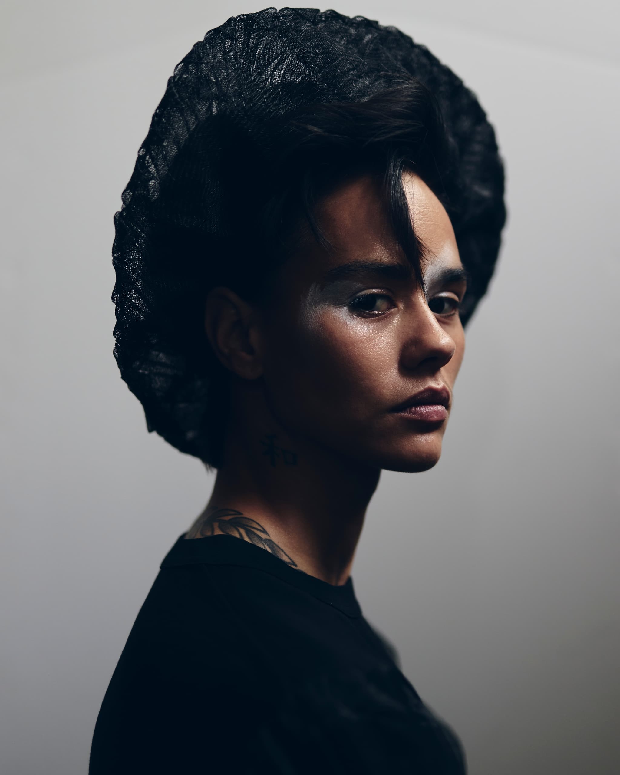 Model in dramatic lighting wearing a black hat with artistic makeup.