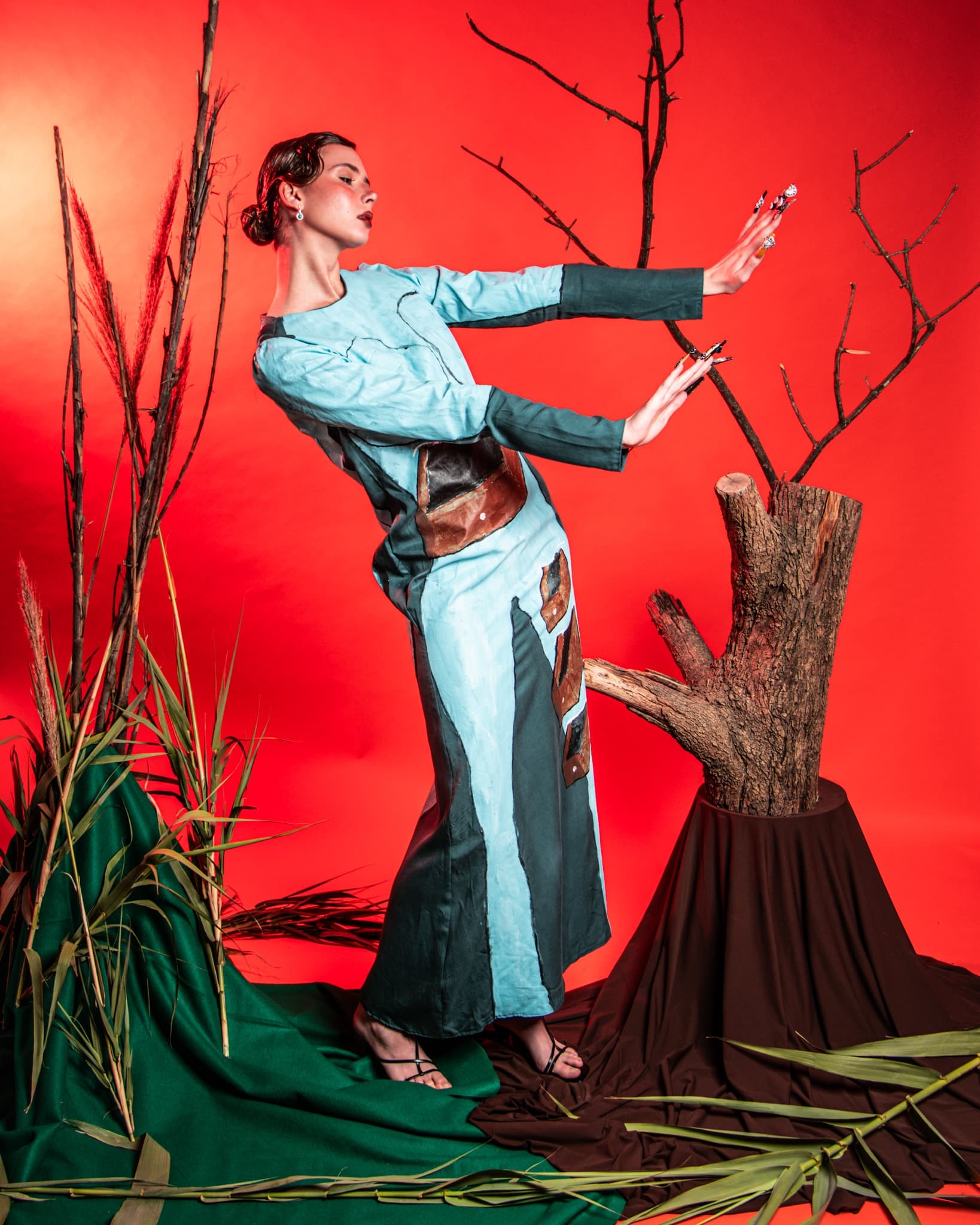 Fashion model poses against bright red background, wearing a unique blue dress.
