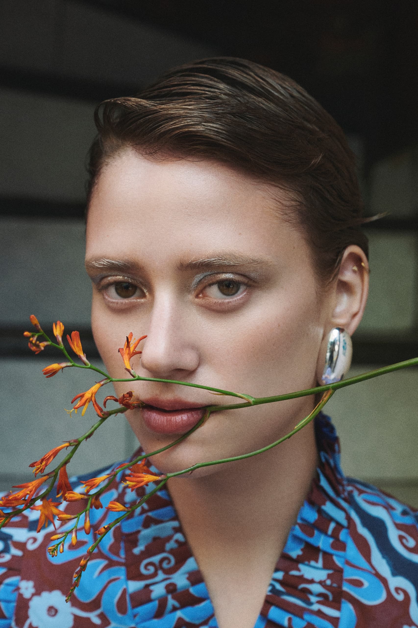 Woman with orange flowers wearing a patterned outfit and silver earring.