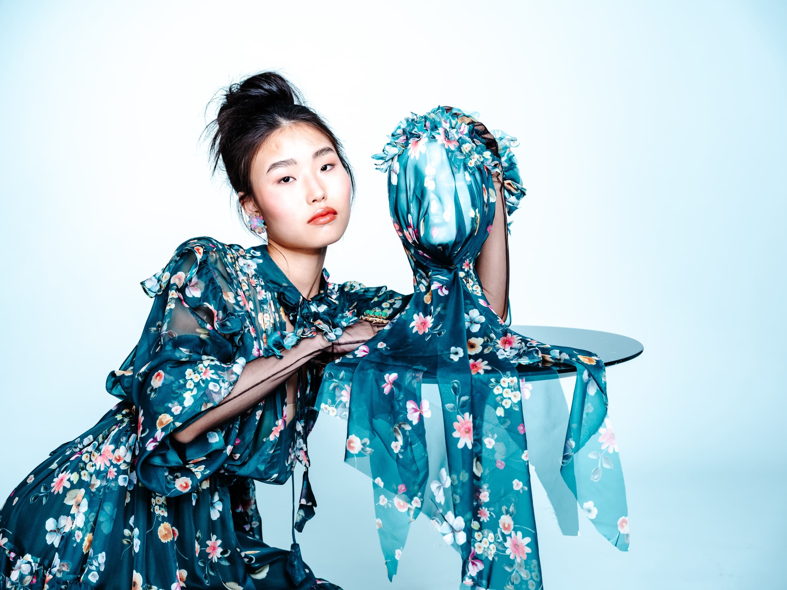 Woman in floral dress posing artistically with matching fabric headpiece.