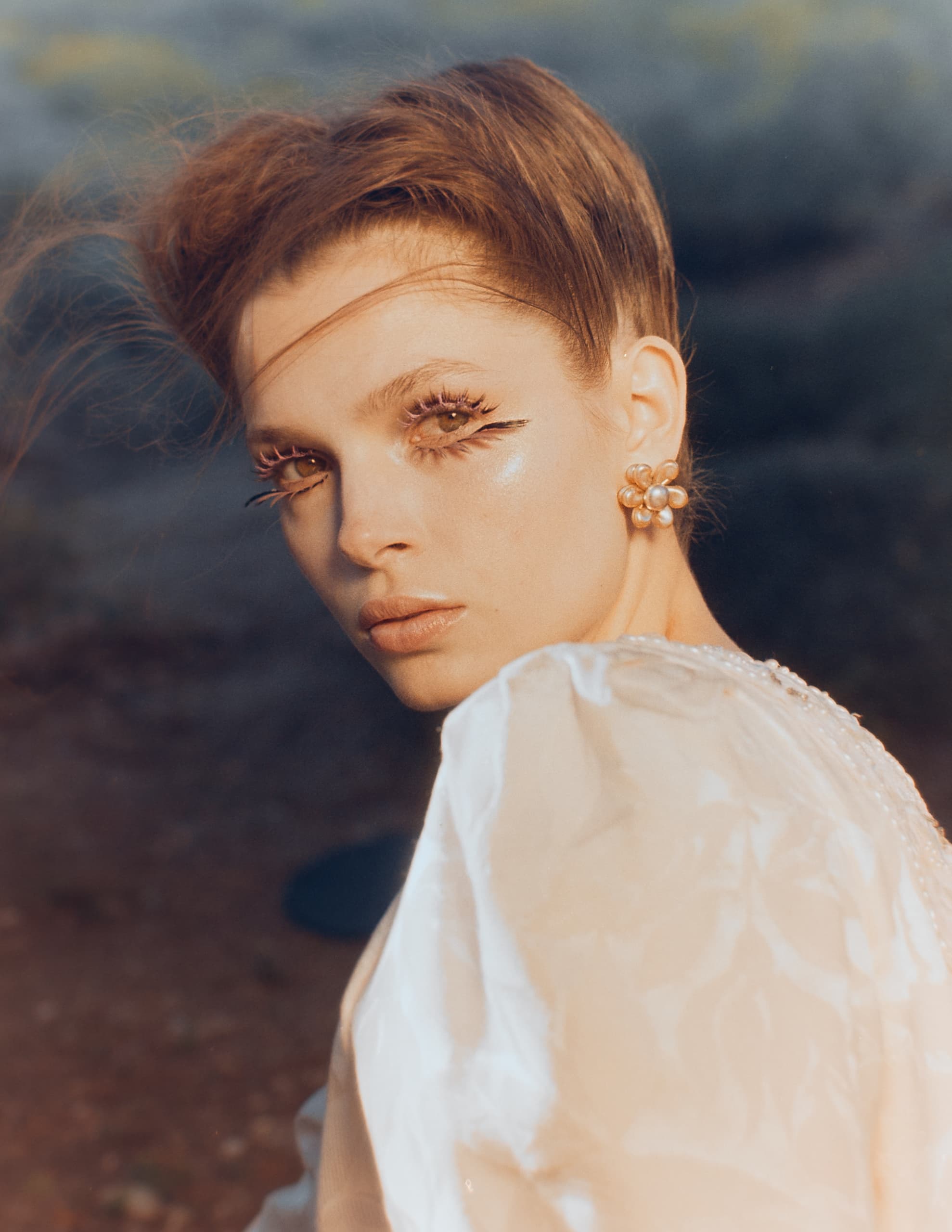 Woman in elegant attire with artistic eye makeup outdoors.