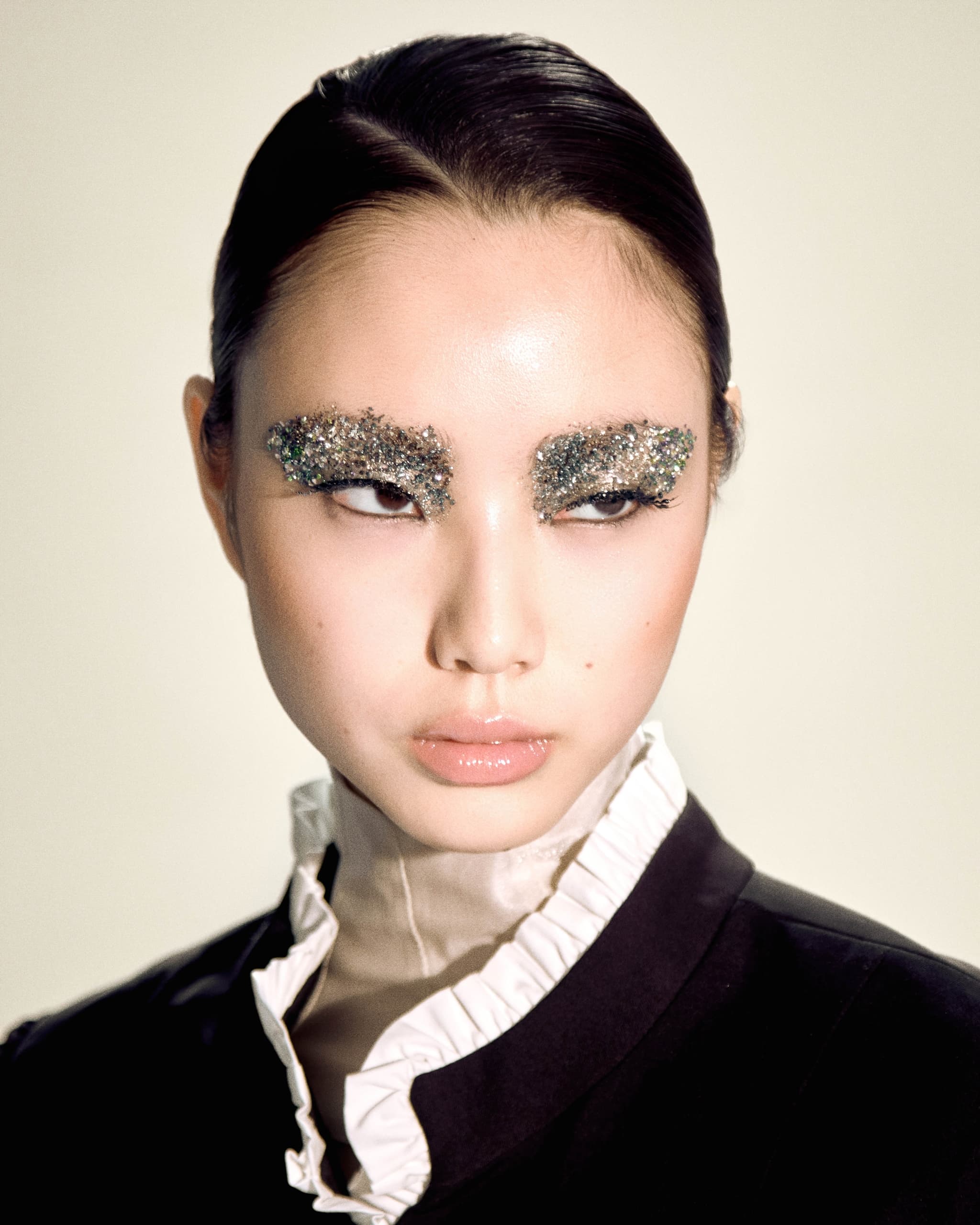 Model with glitter eyebrows, sleek hair, and a formal black and white outfit.