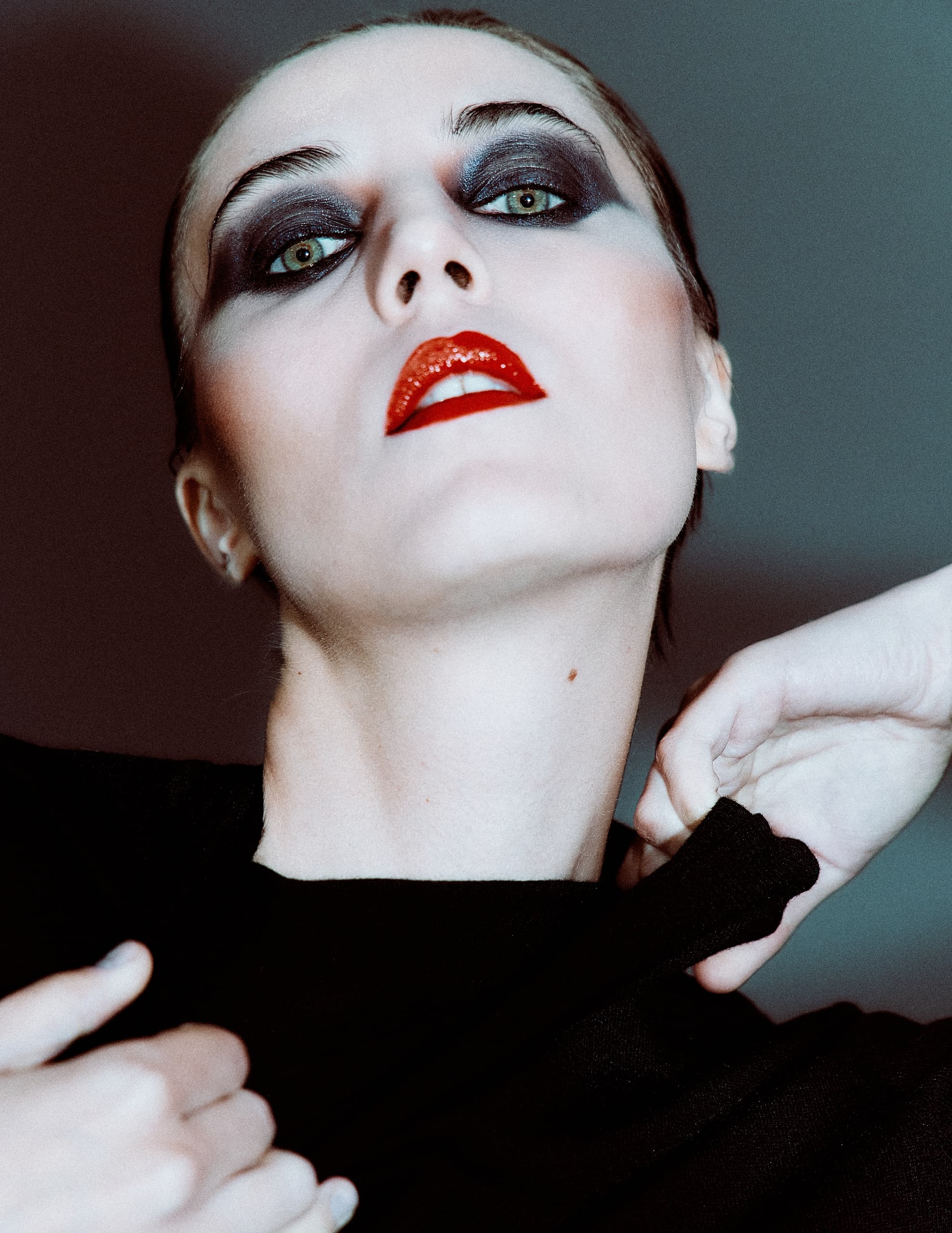 Dramatic makeup with bold eyes and red lips, striking pose against dark background.