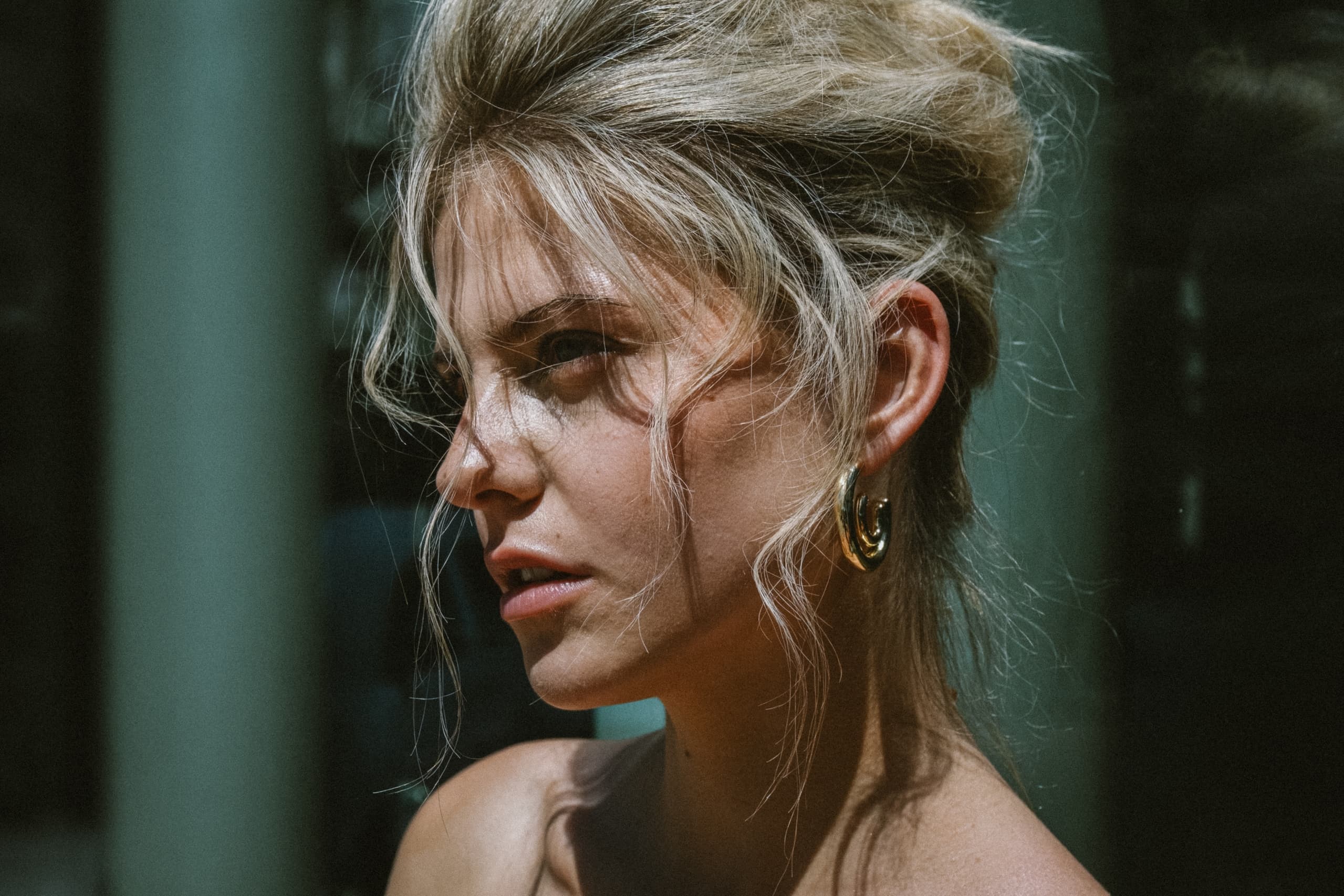 Portrait of a woman with messy hair and gold earrings in natural light.