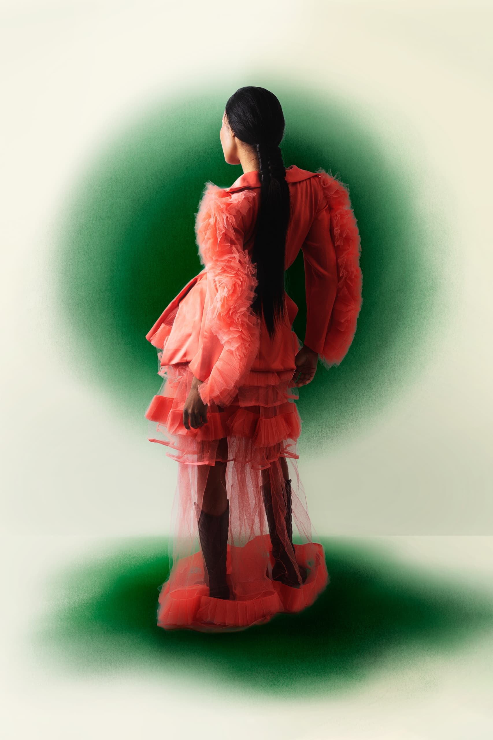 Woman in layered pink dress with green background, showcasing modern fashion style.