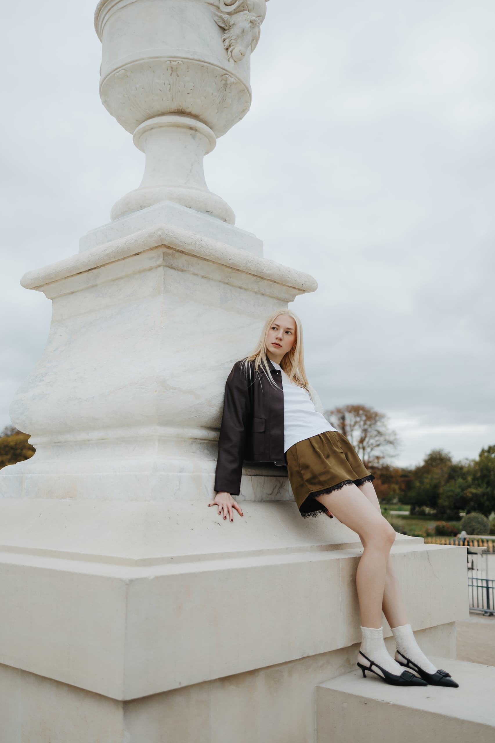 Fashionable woman leans on large stone monument outdoors.