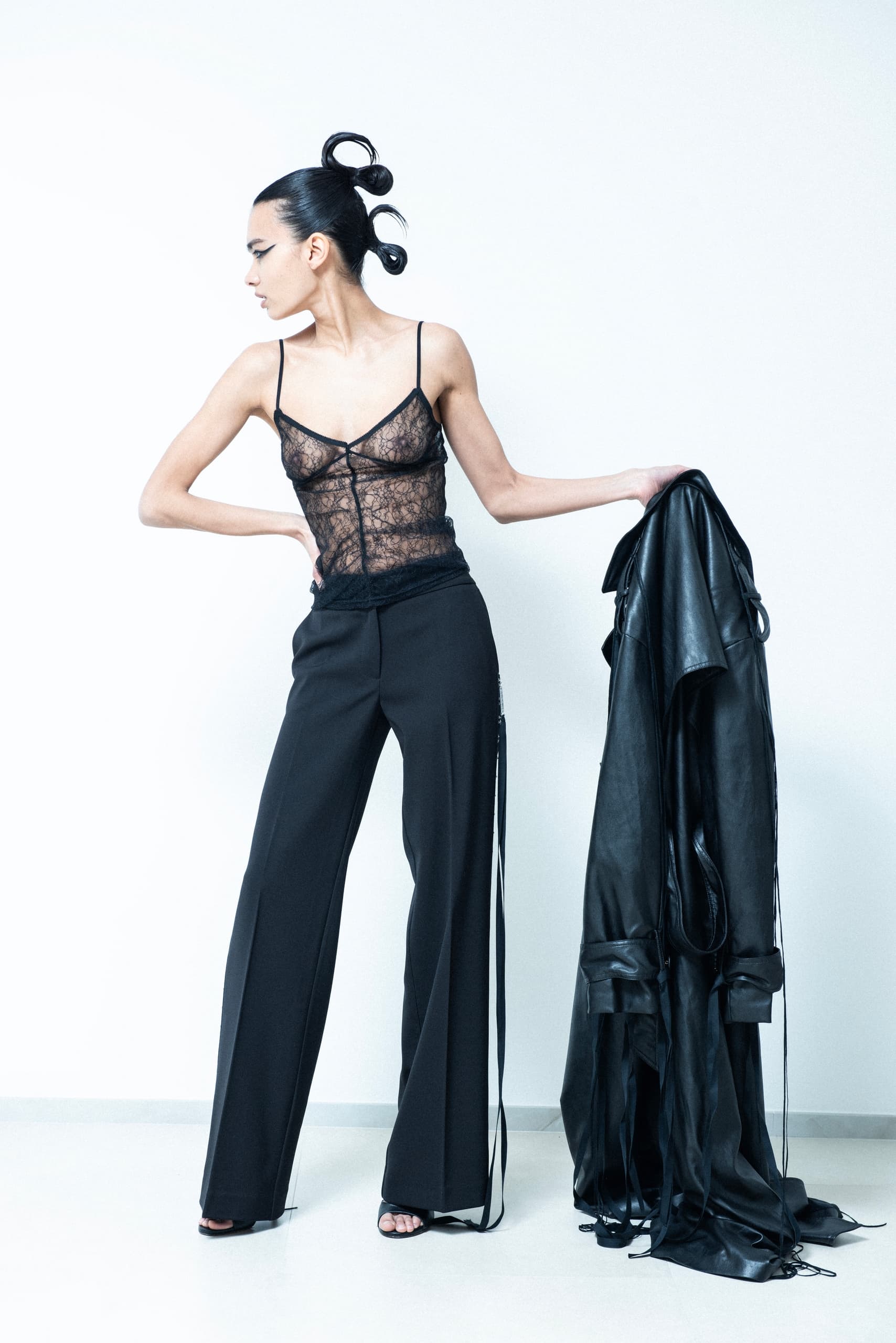 Fashion model in lace top and black pants holding leather jacket.