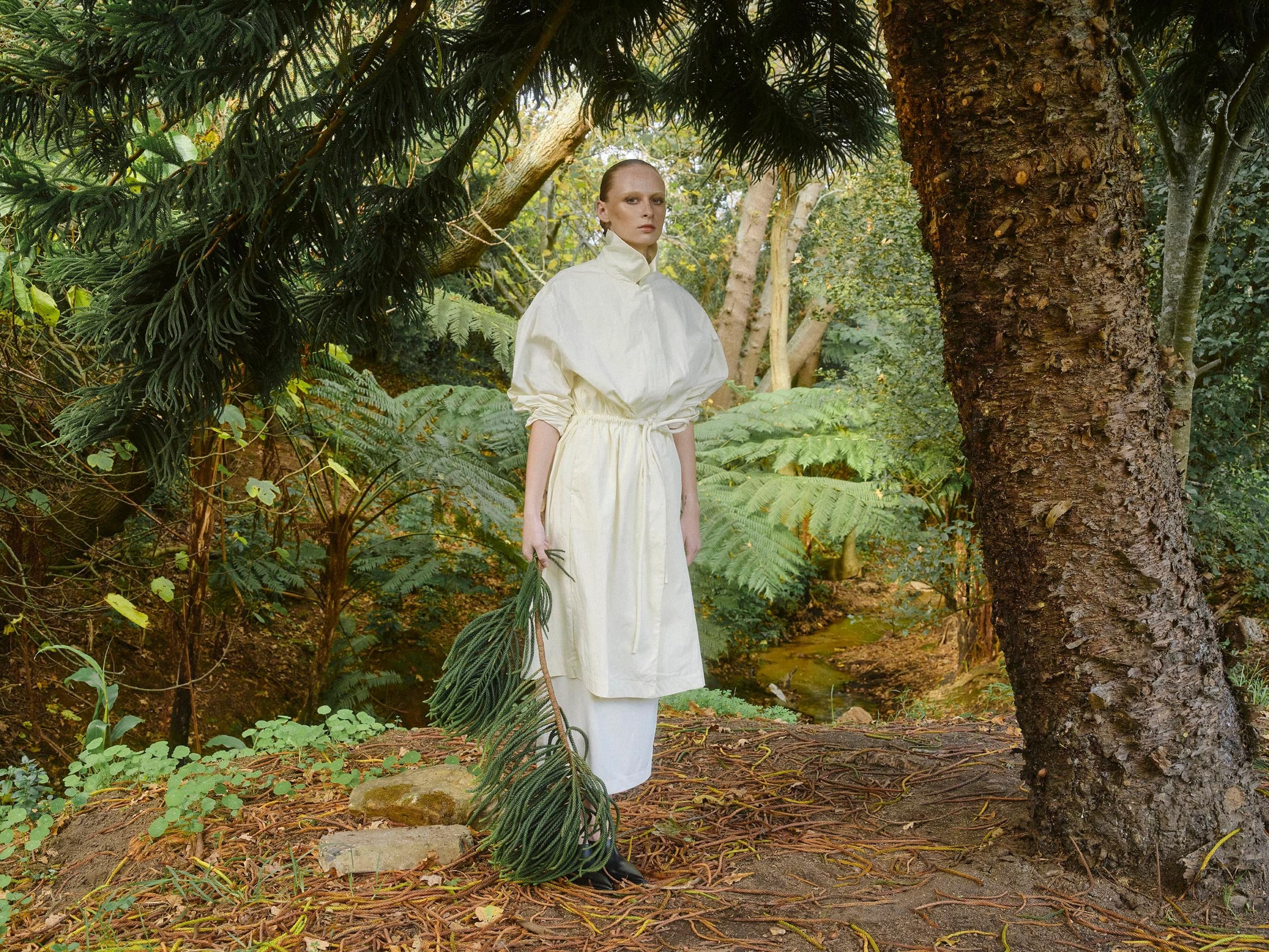 Person in white dress exploring a lush, green forest.