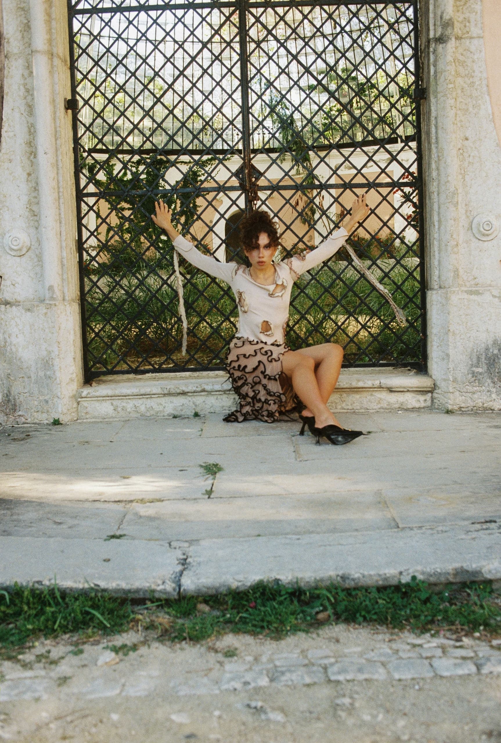 Fashionable woman poses by ornate metal gate outdoors.
