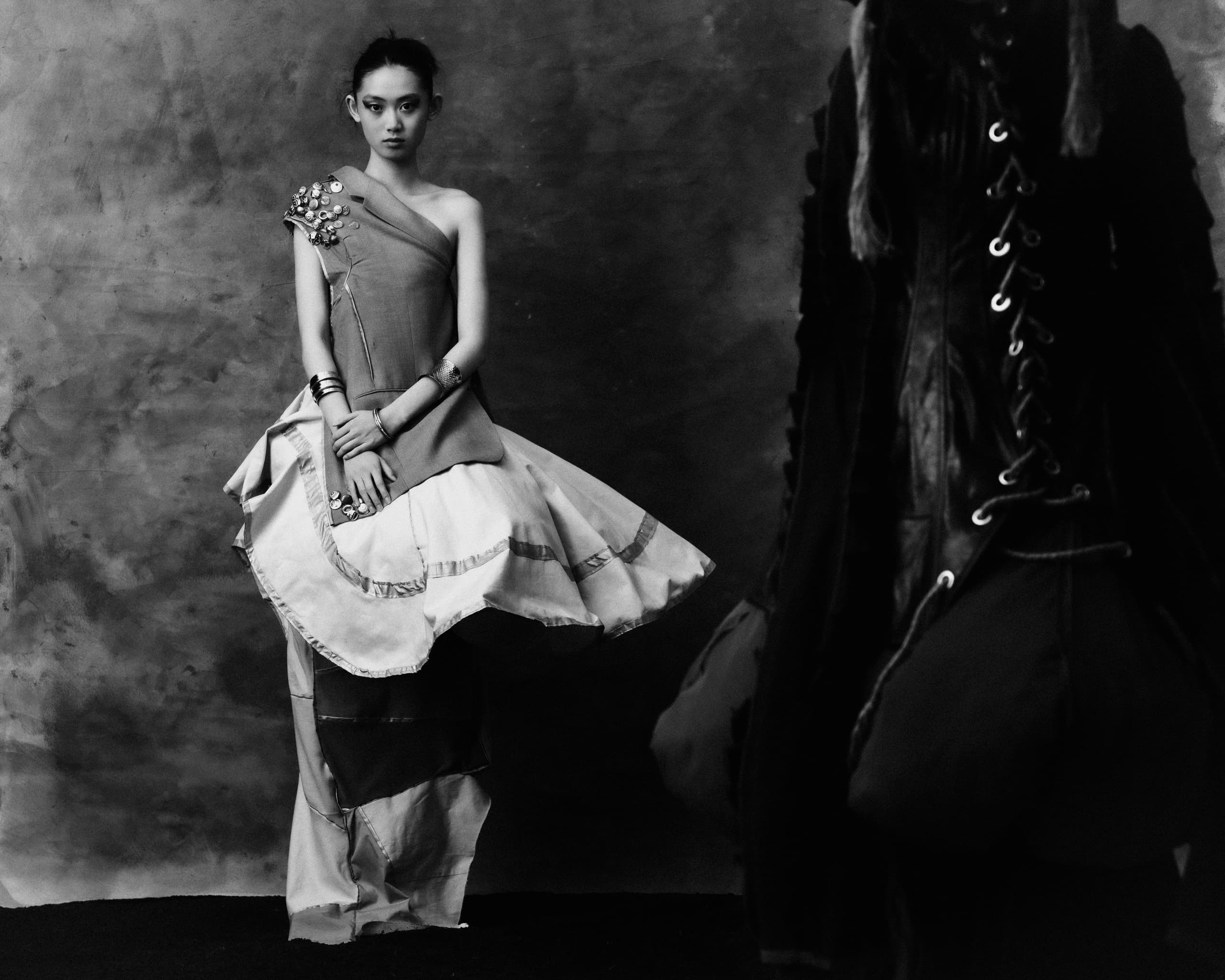 Artistic black and white fashion portrait with layered dress and textured backdrop.