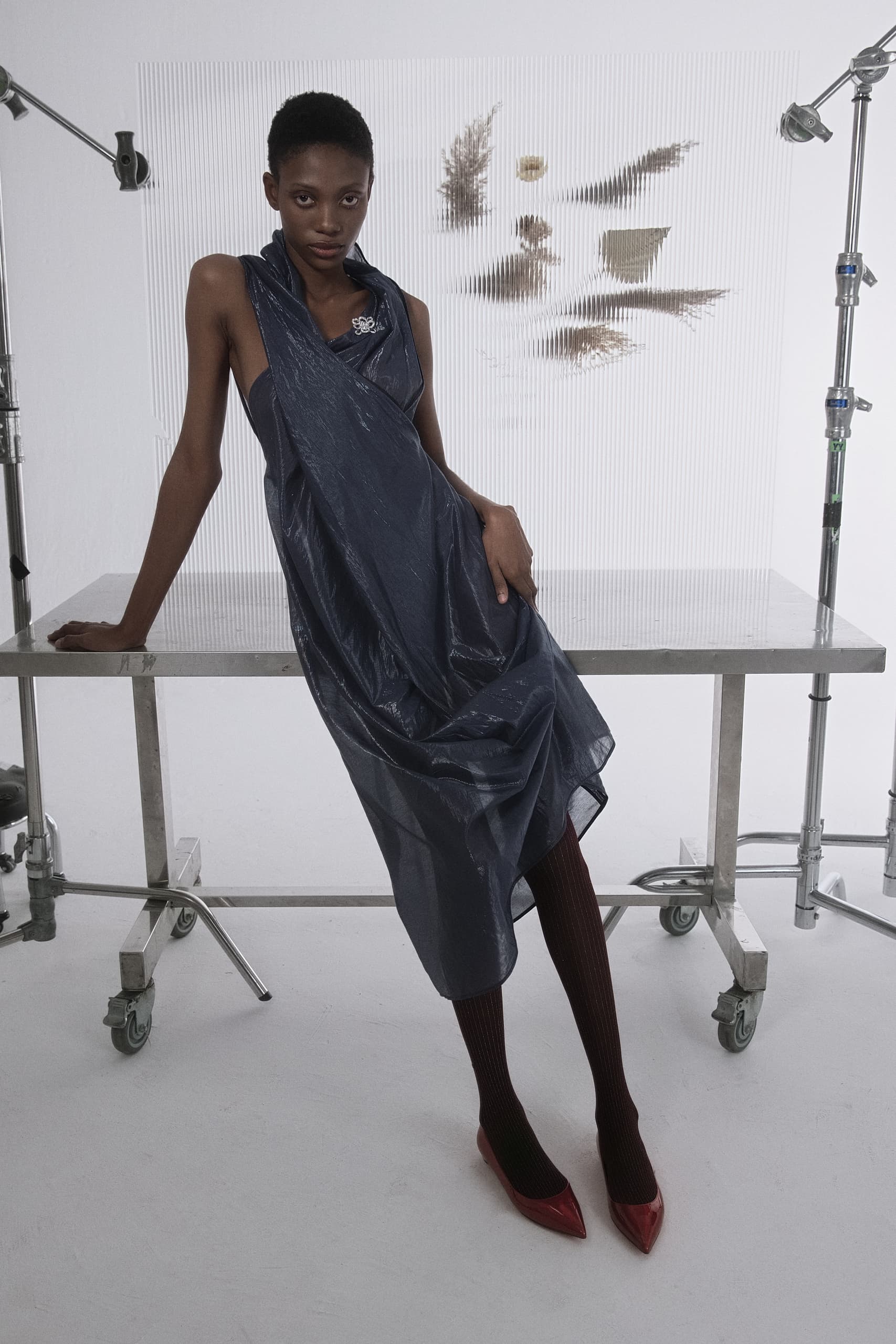 Model in stylish gray dress and red shoes in a studio photoshoot setting.