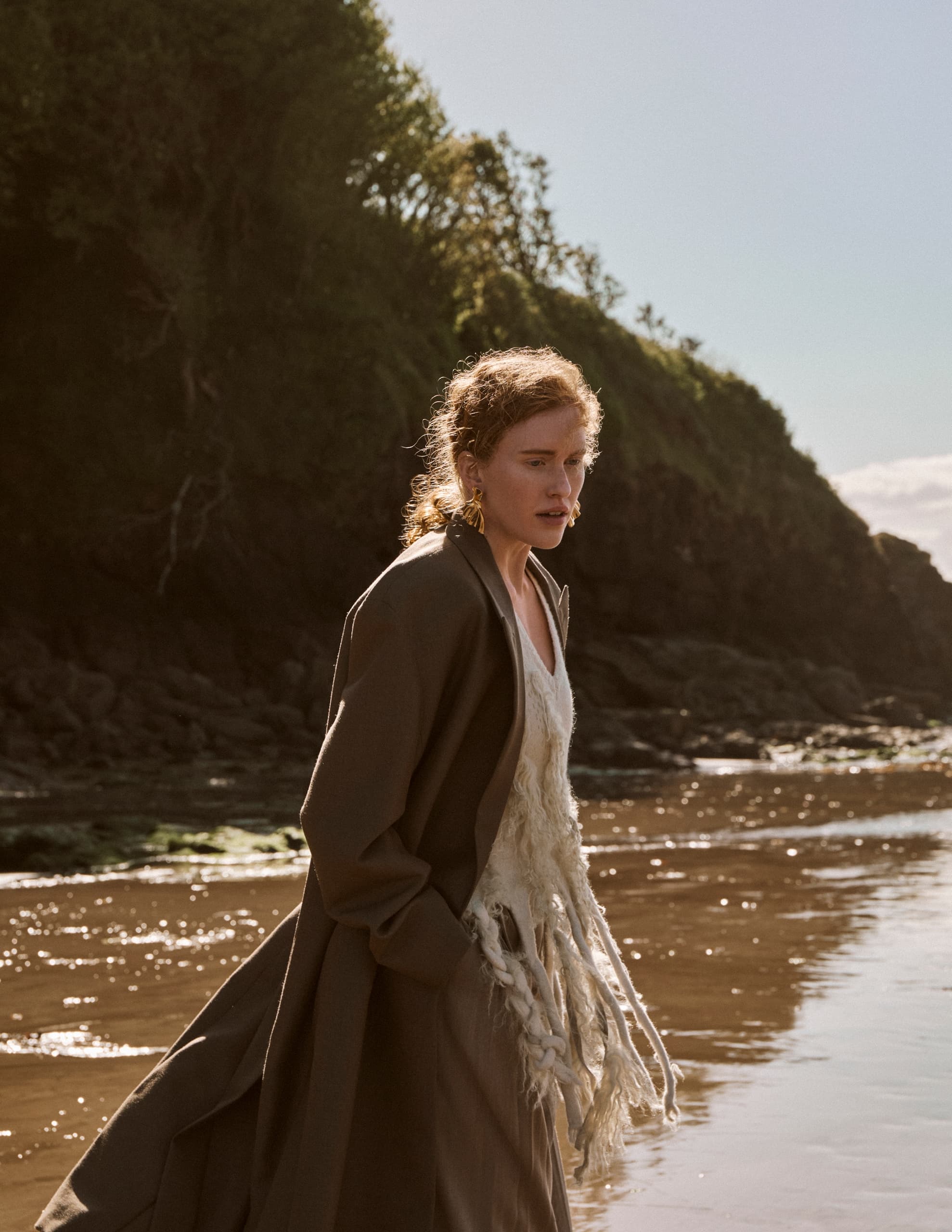 Woman walking on serene beach with cliffs in the background.