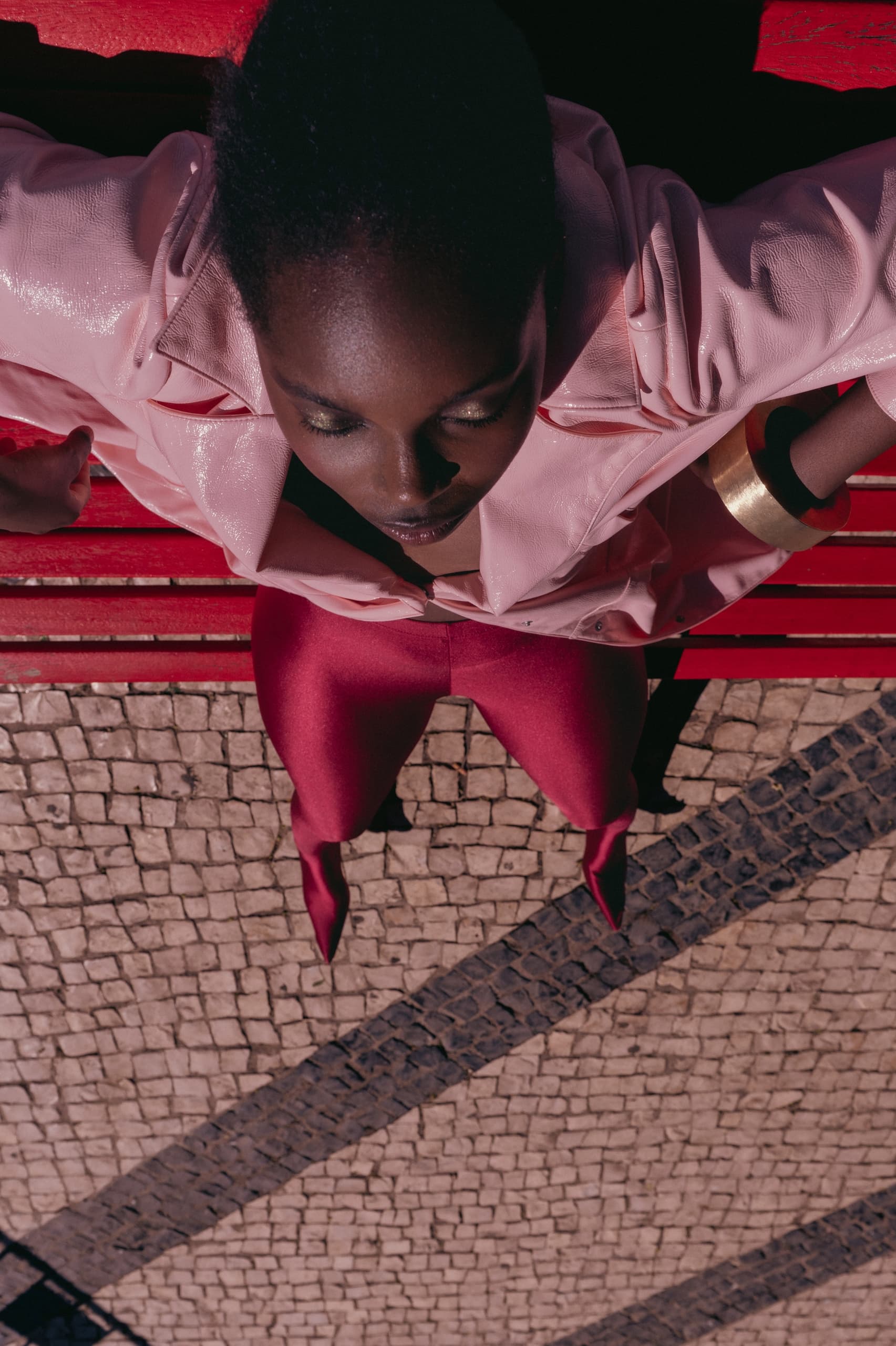 Person in pink and red fashion, sitting on a bench, viewed from above.