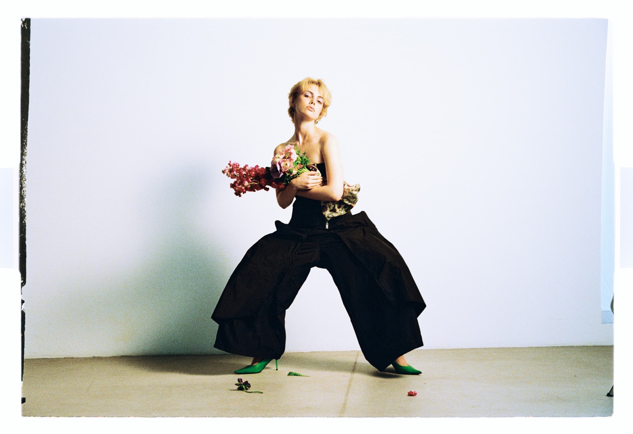 Person in avant-garde attire holding flowers against a minimalistic backdrop.