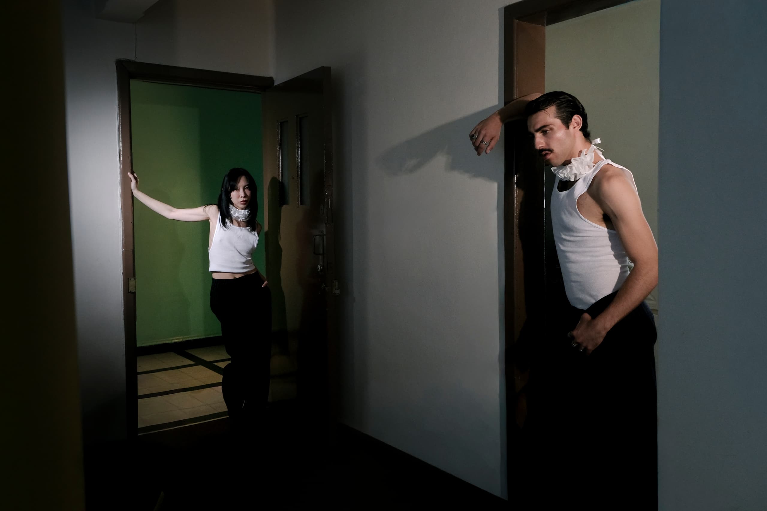 Two people in stylish outfits pose in doorways with dramatic lighting.