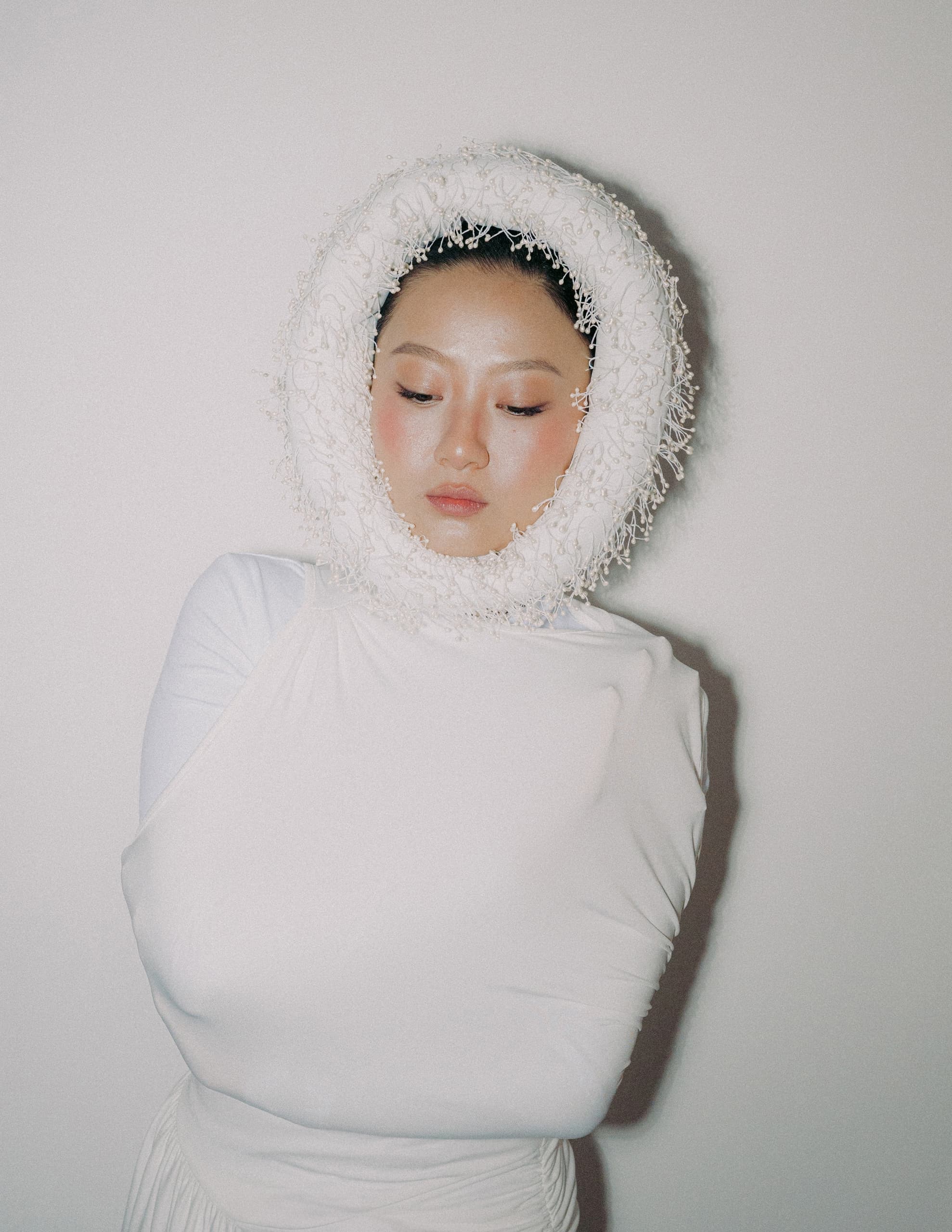 Person in white avant-garde outfit with textured circular headpiece.