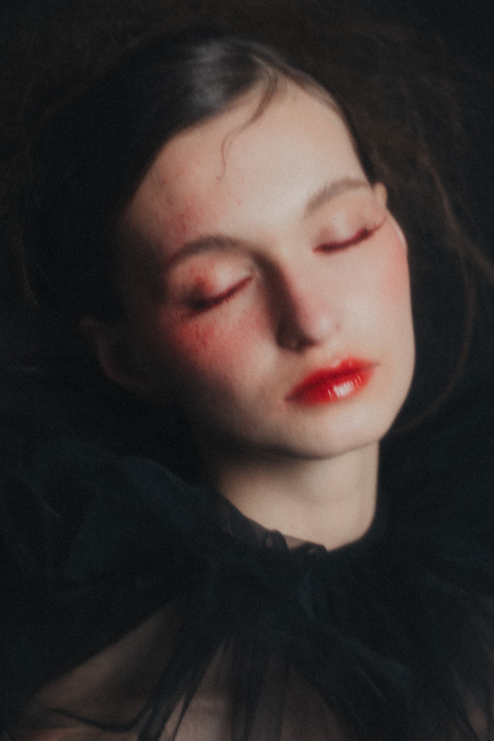 Dreamy portrait with blush makeup, closed eyes, and glossy red lips in soft focus.