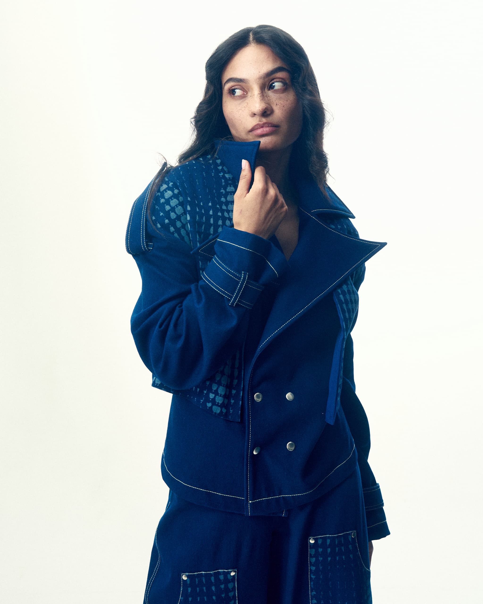 Woman in blue denim jacket with patterned panels, posing stylishly against white backdrop.