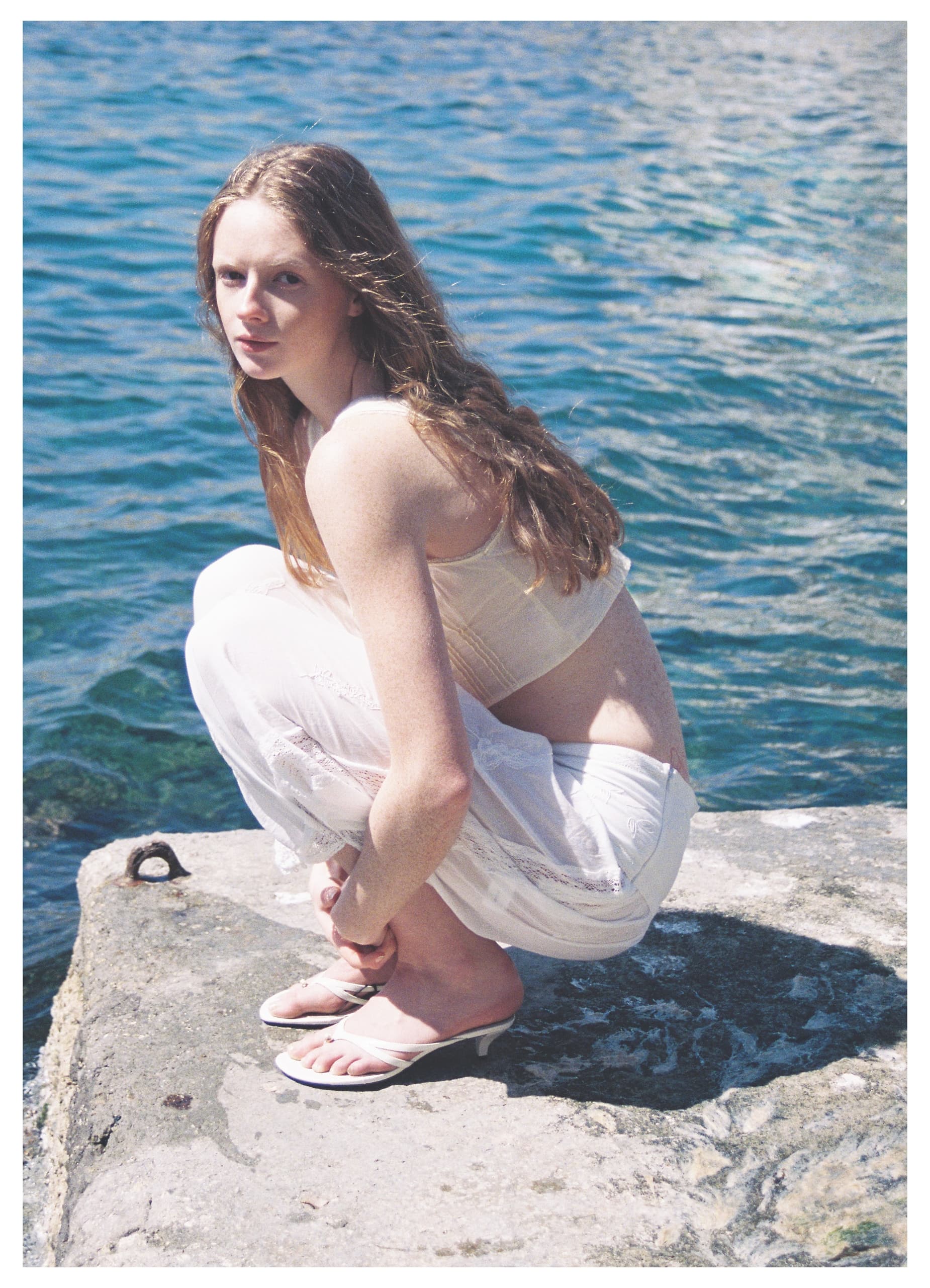 Woman in white dress sitting by the sea on a sunny day.