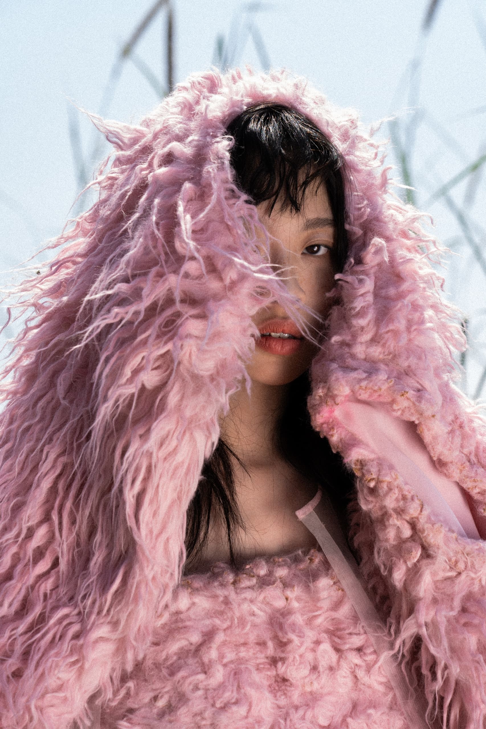 Model in a pink furry outfit, peeks through stylish fashion ensemble.