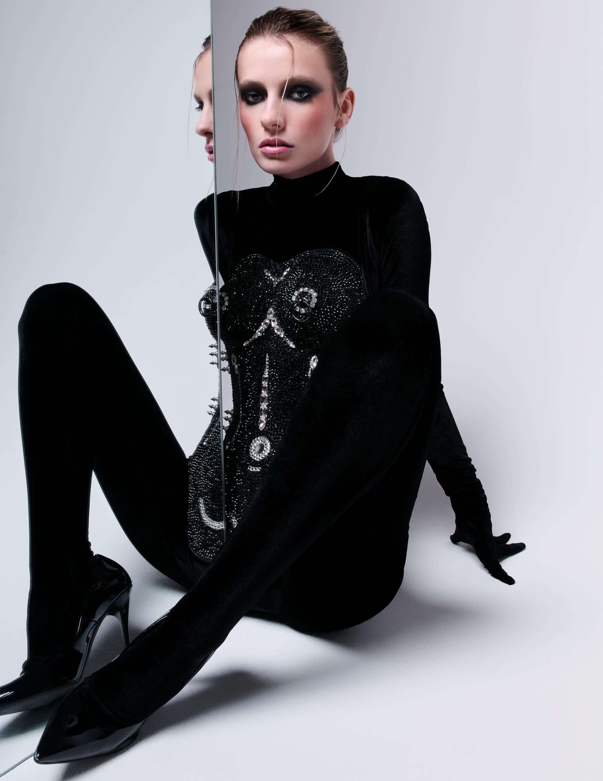 Fashion model in black bodysuit sitting by a mirror, dramatic makeup.