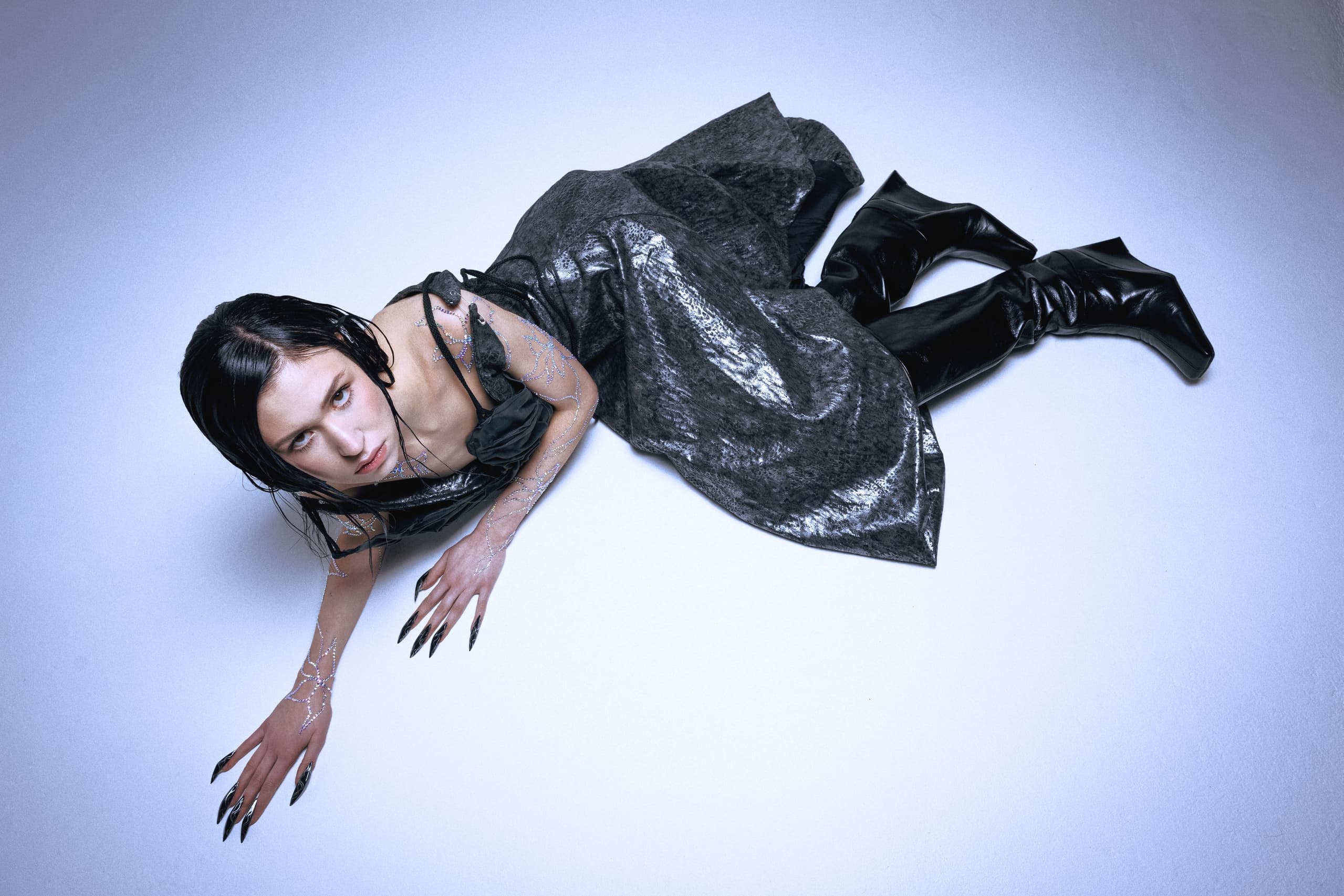 Woman in futuristic black dress lying on floor, artistic pose.