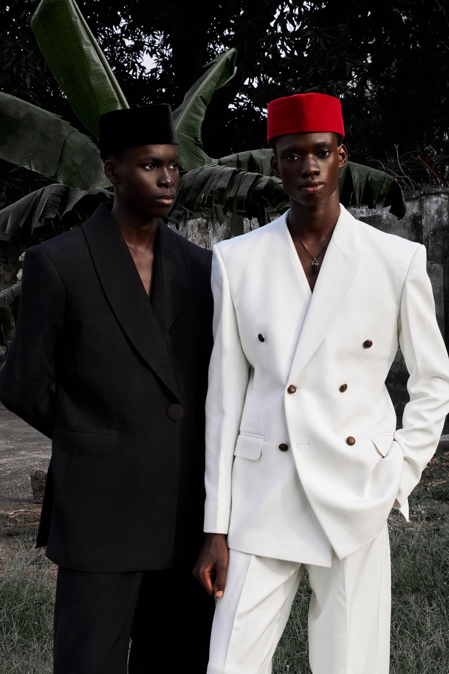 Two men in stylish black and white suits with hats, standing outdoors.