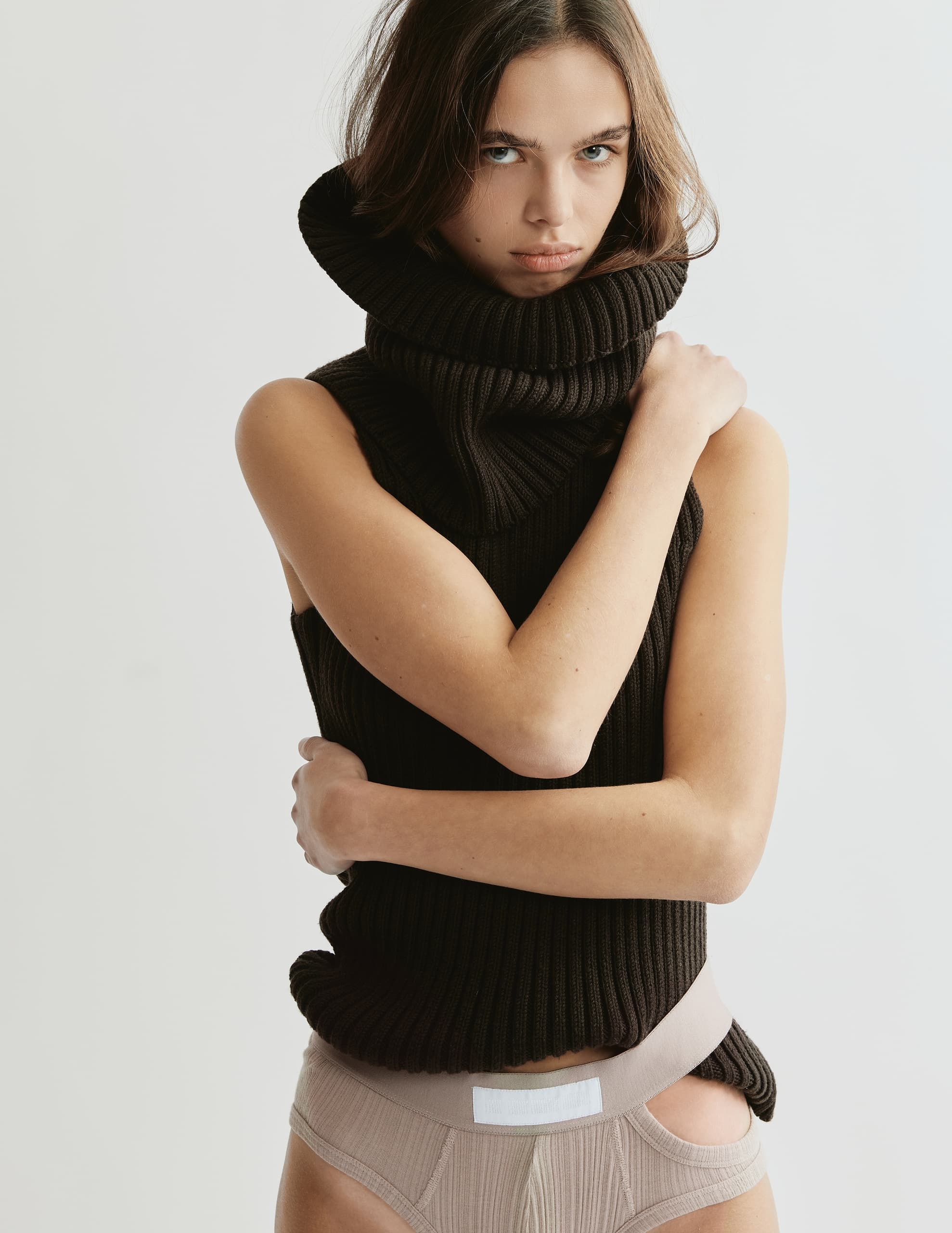 Woman posing in black sleeveless turtleneck and beige shorts against white background.