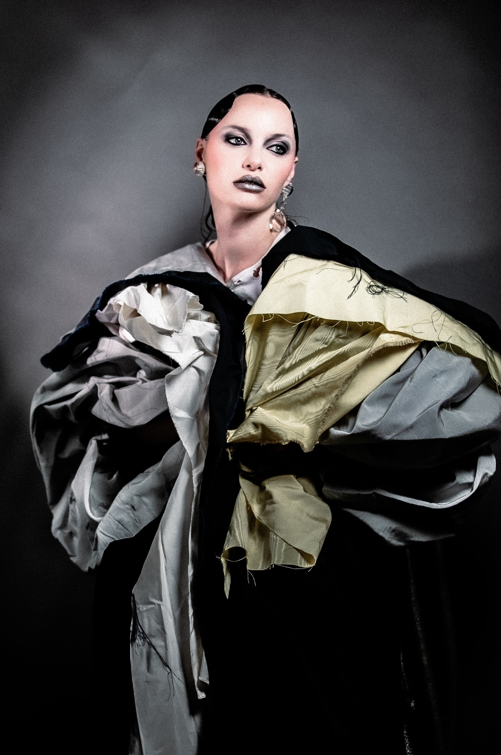 Avant-garde fashion with bold makeup and layered fabrics in a striking portrait.
