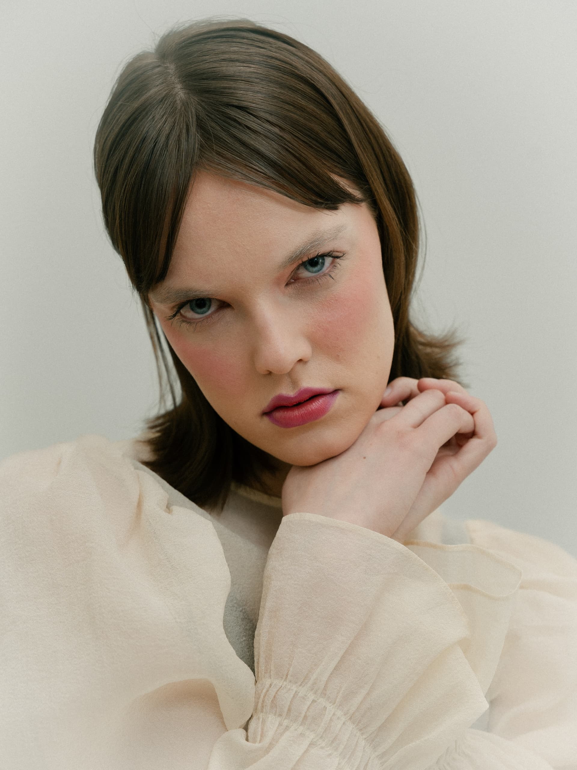 Portrait of a thoughtful woman with light blouse and soft makeup.