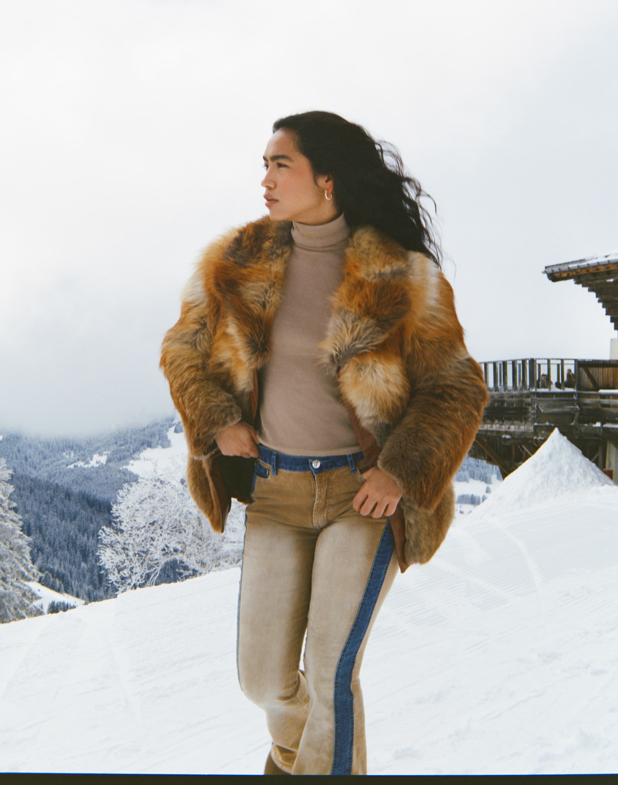 Person wearing fur coat in snowy mountain landscape.