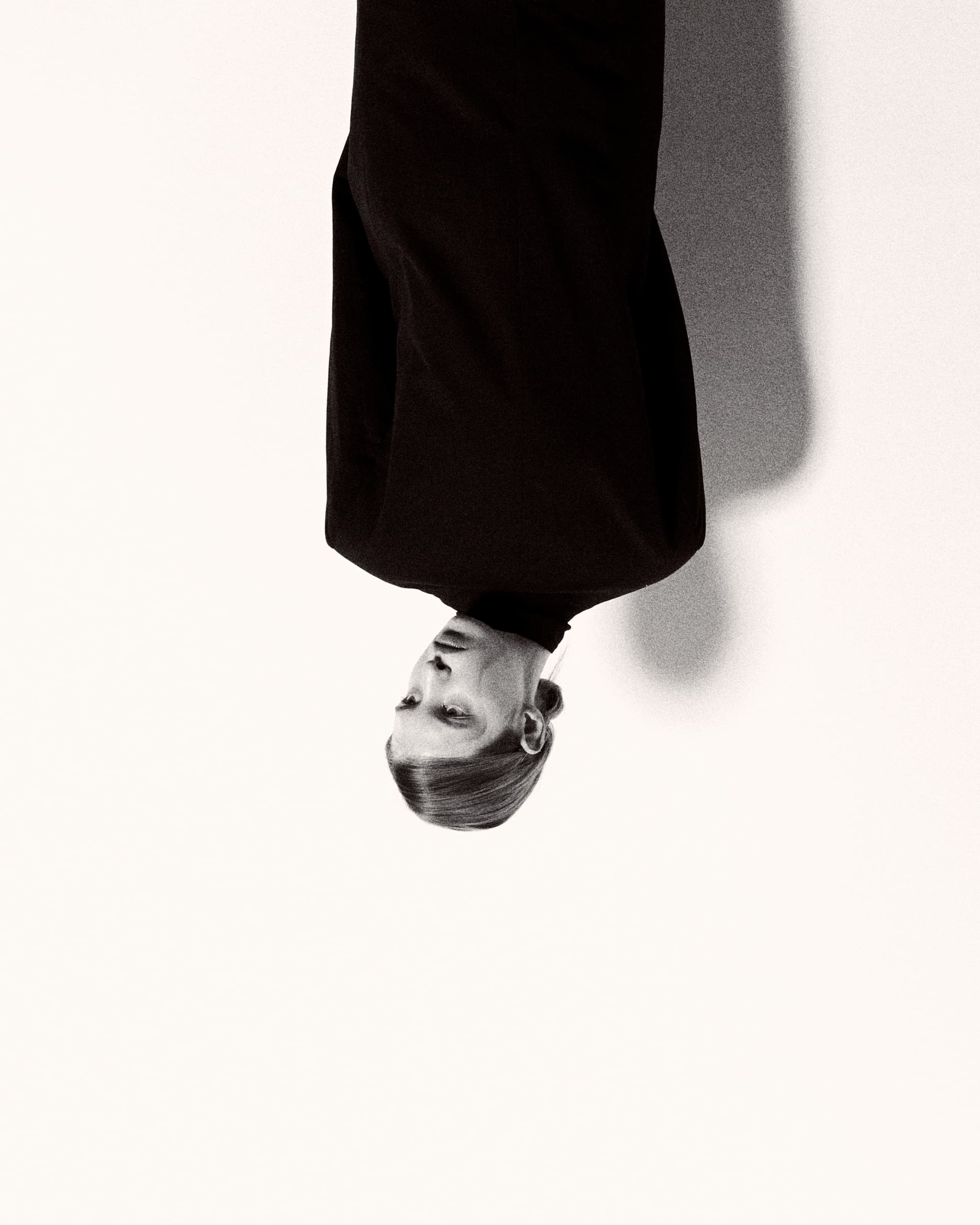 Upside-down portrait, person in black attire against light background, minimalist style.