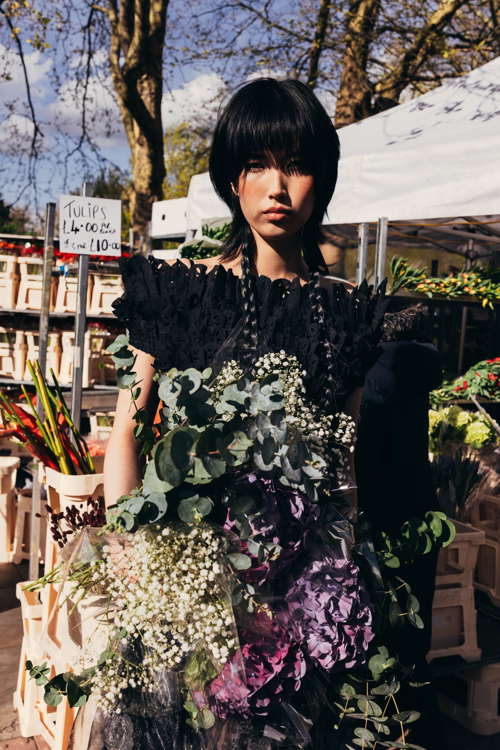 Woman in black dress holding flowers at an outdoor market.
