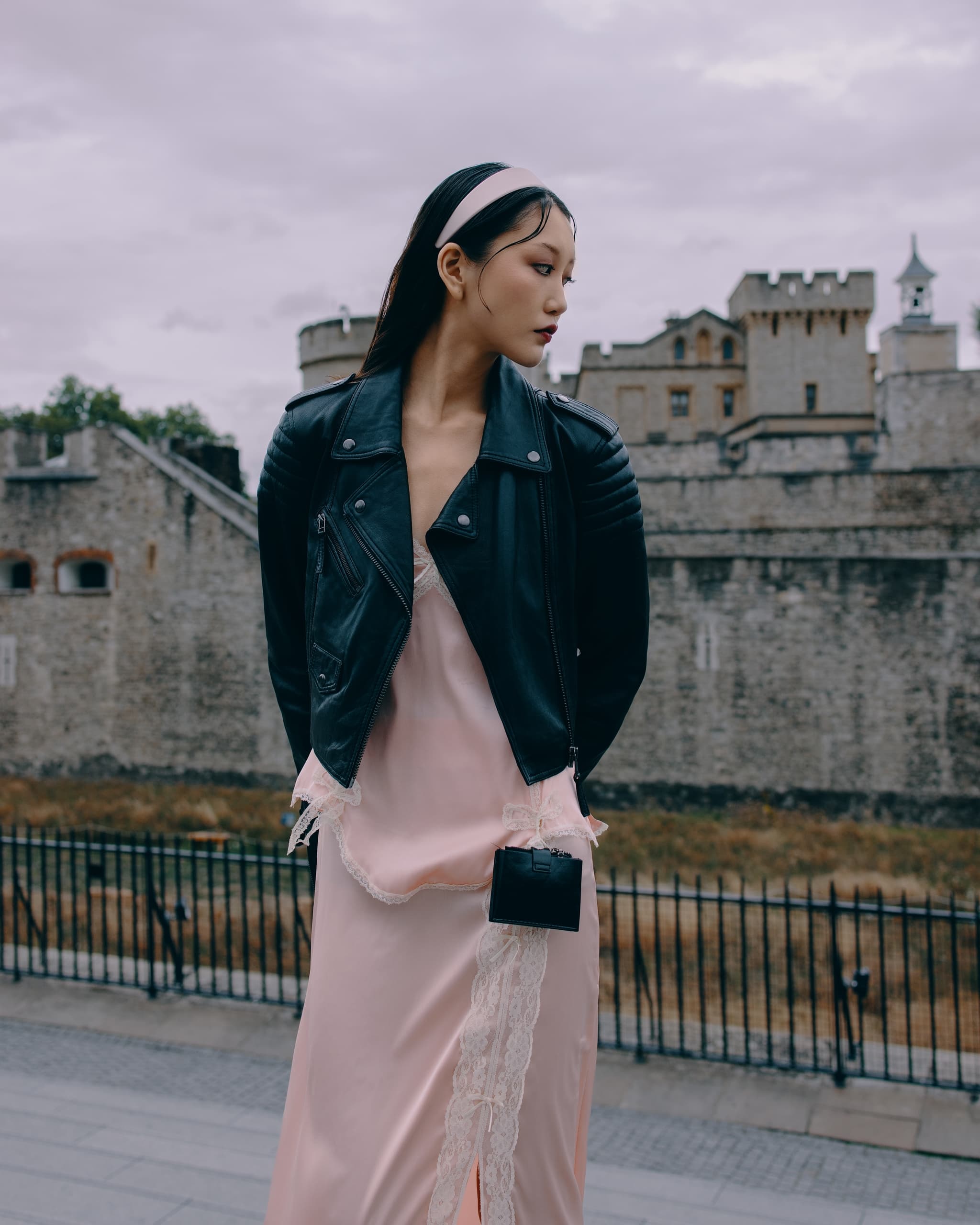 Stylish woman in pink dress and leather jacket at historic stone building.