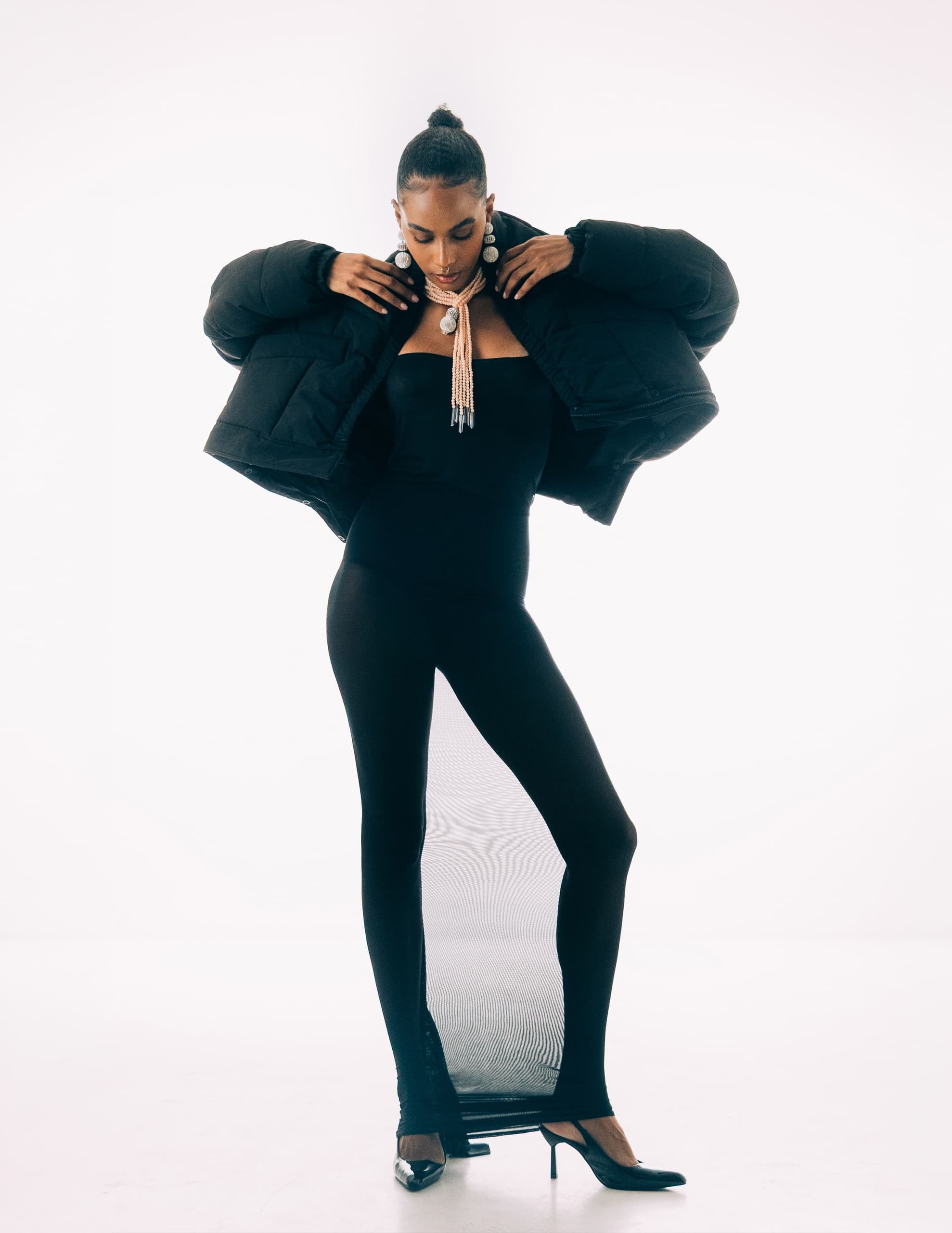 Woman in black outfit and jacket, striking a pose in stylish high heels.