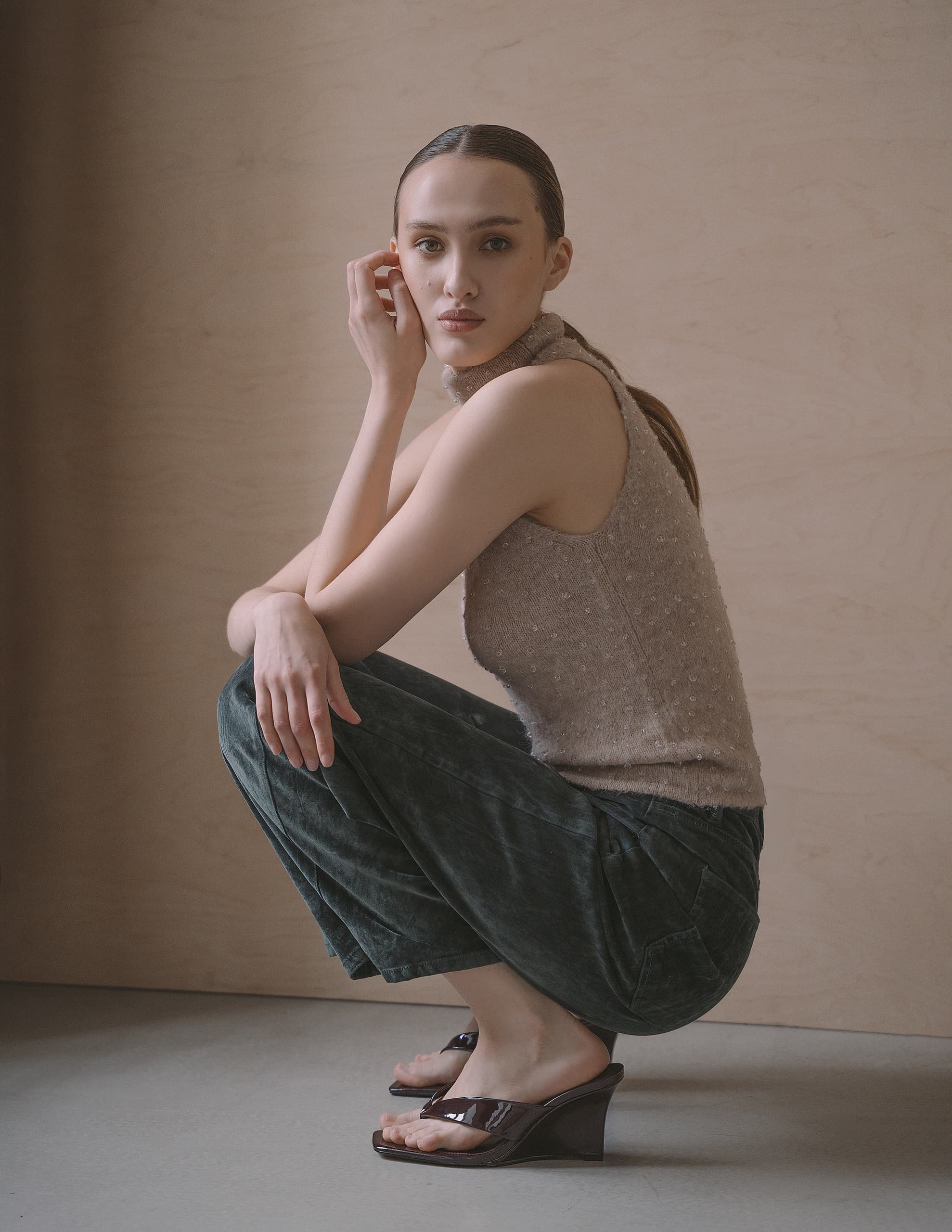 Woman in stylish outfit squatting, wearing sleeveless top and dark pants.