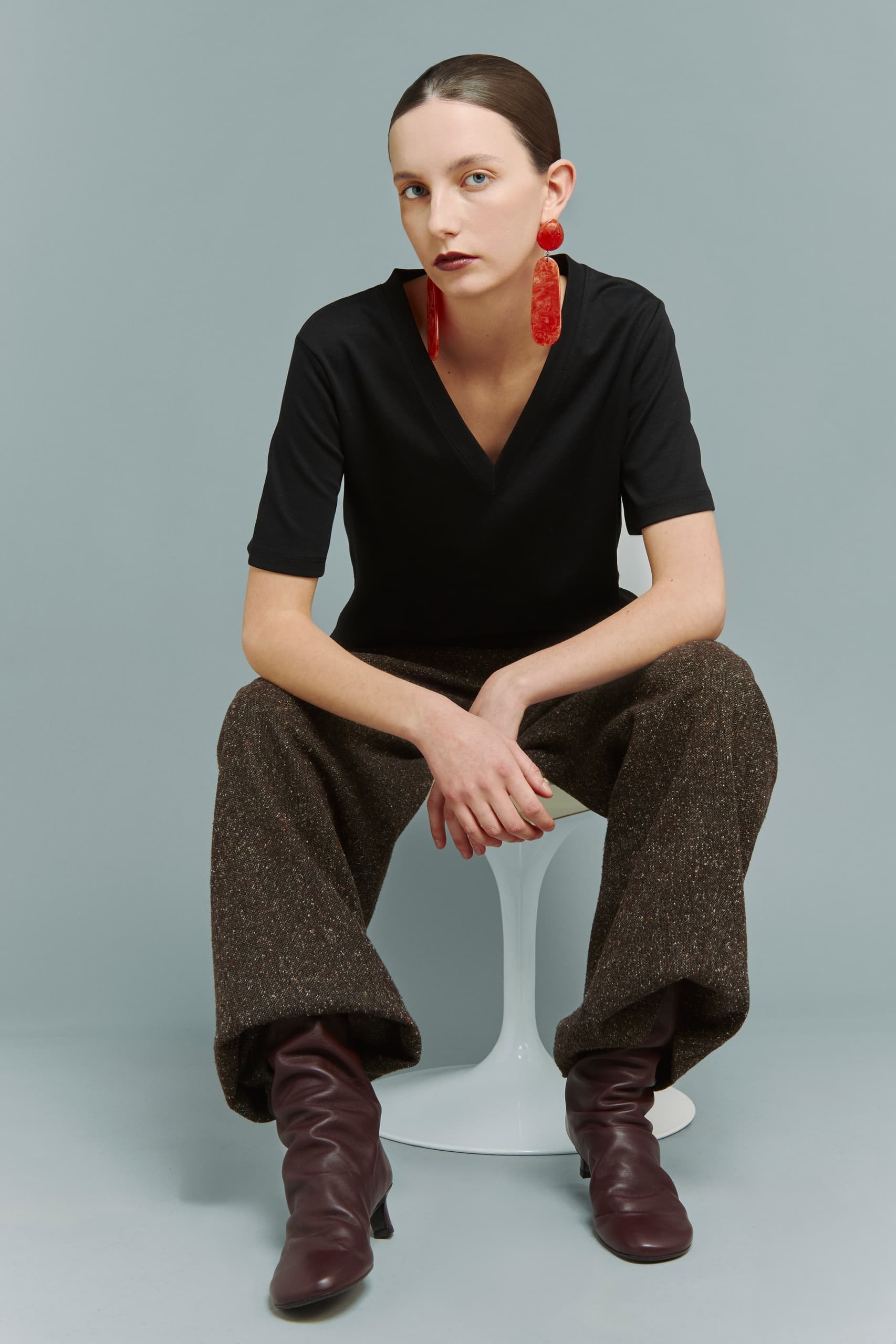 Fashionable woman in black top and red earrings, seated on modern chair.