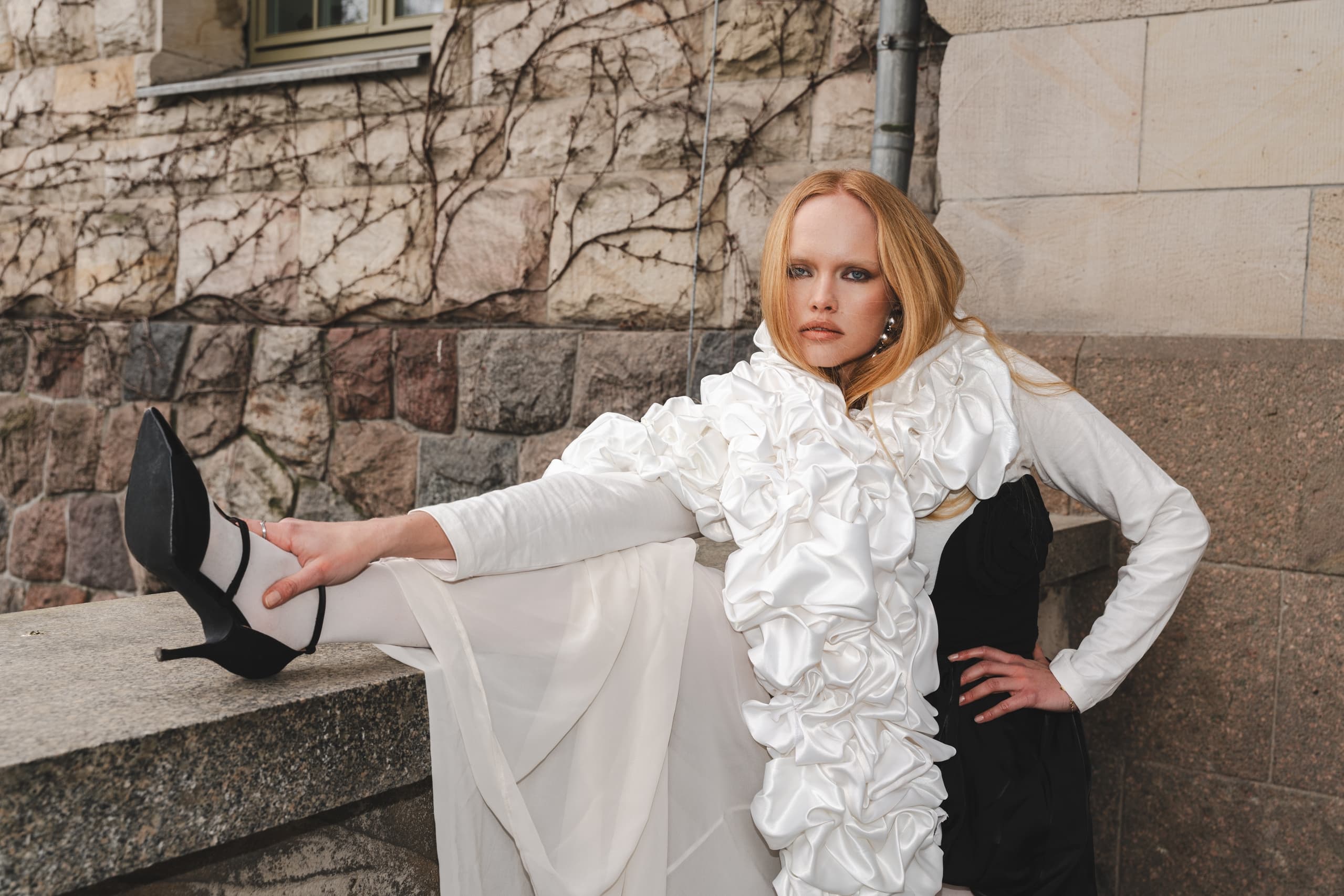Fashionable woman in a ruffled outfit poses outdoors on stone steps, chic style.