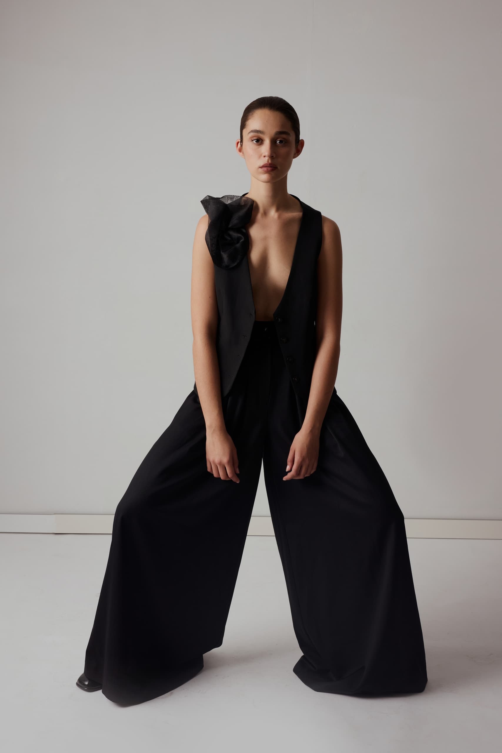 Elegant woman in stylish black outfit, wide pants, minimalist studio.