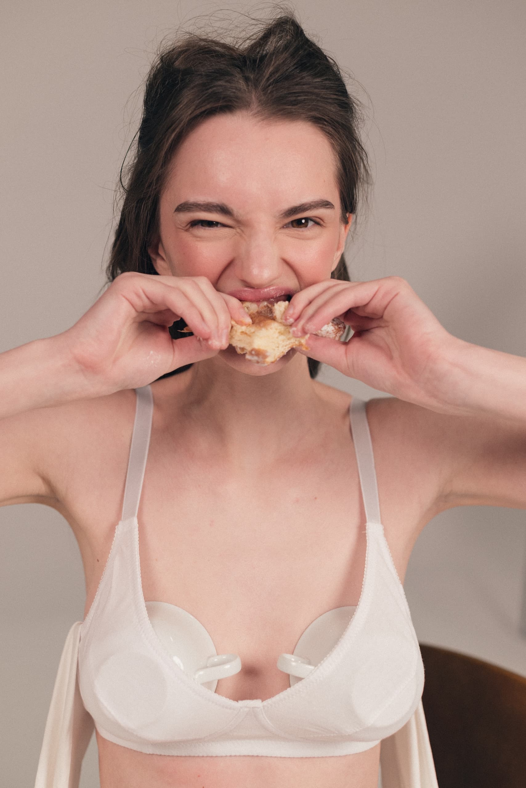 Woman in white bra eating pastry, playful expression.