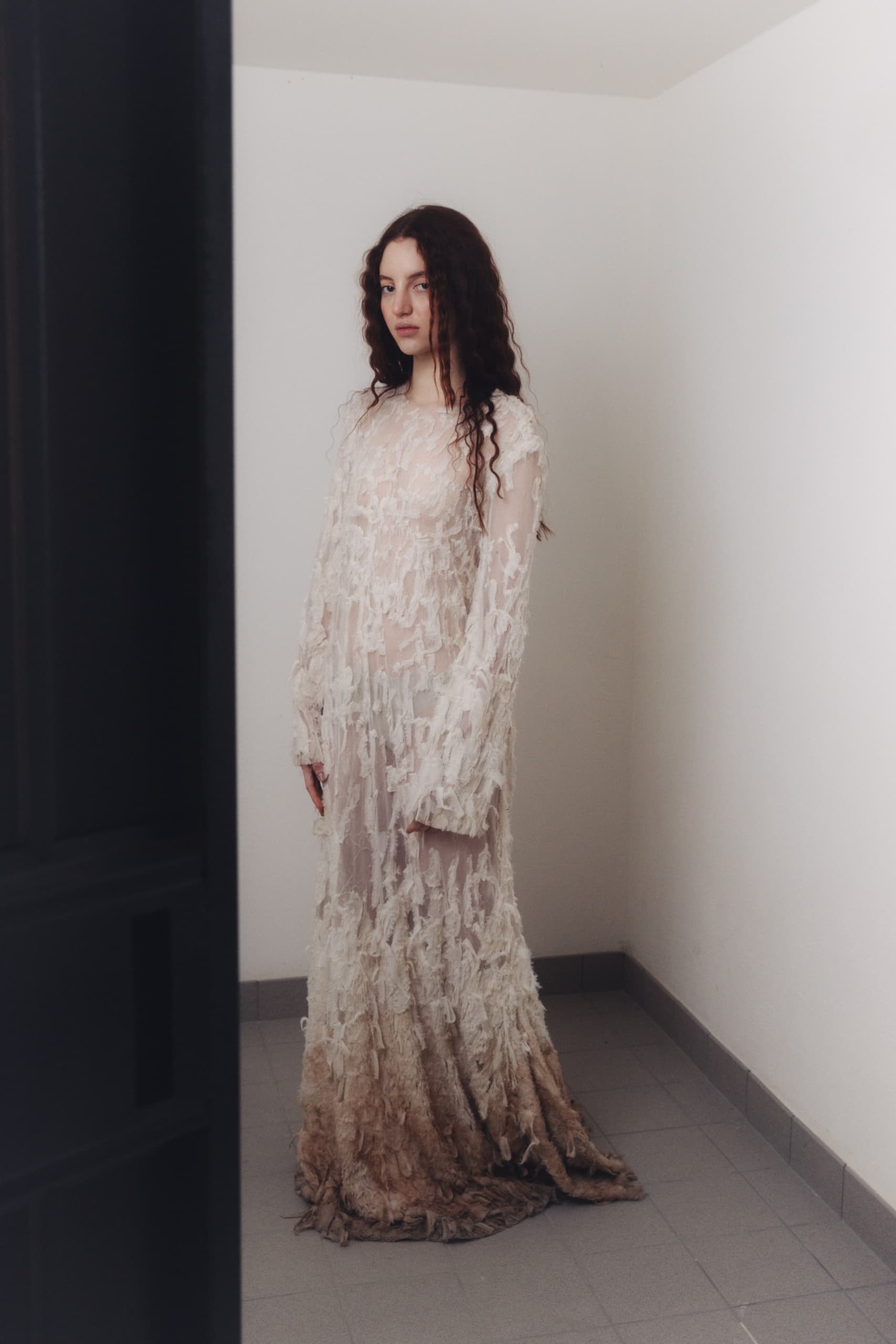 Woman in a textured, ethereal gown standing in a minimalist room.