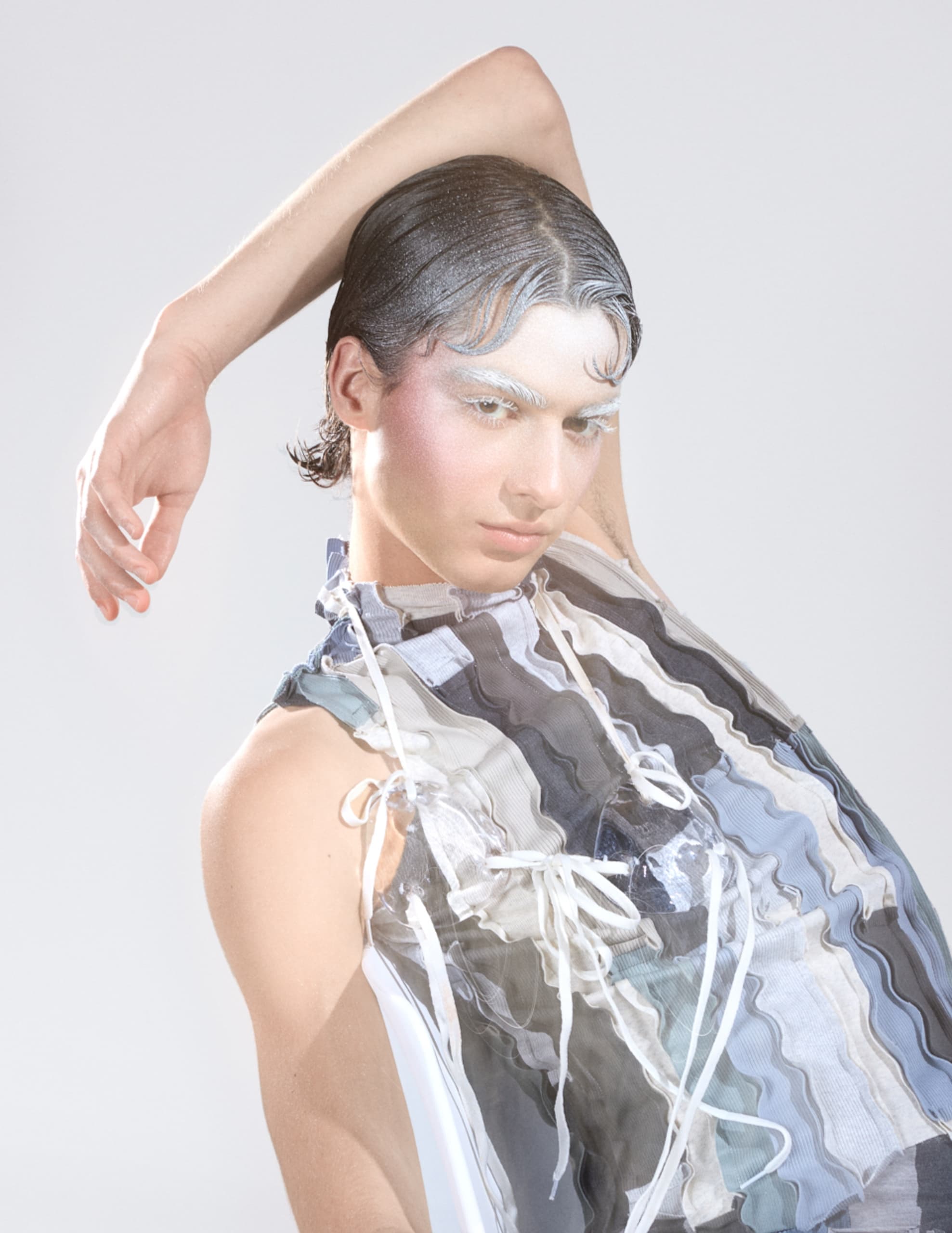Model in avant-garde outfit with artistic makeup against a neutral background.