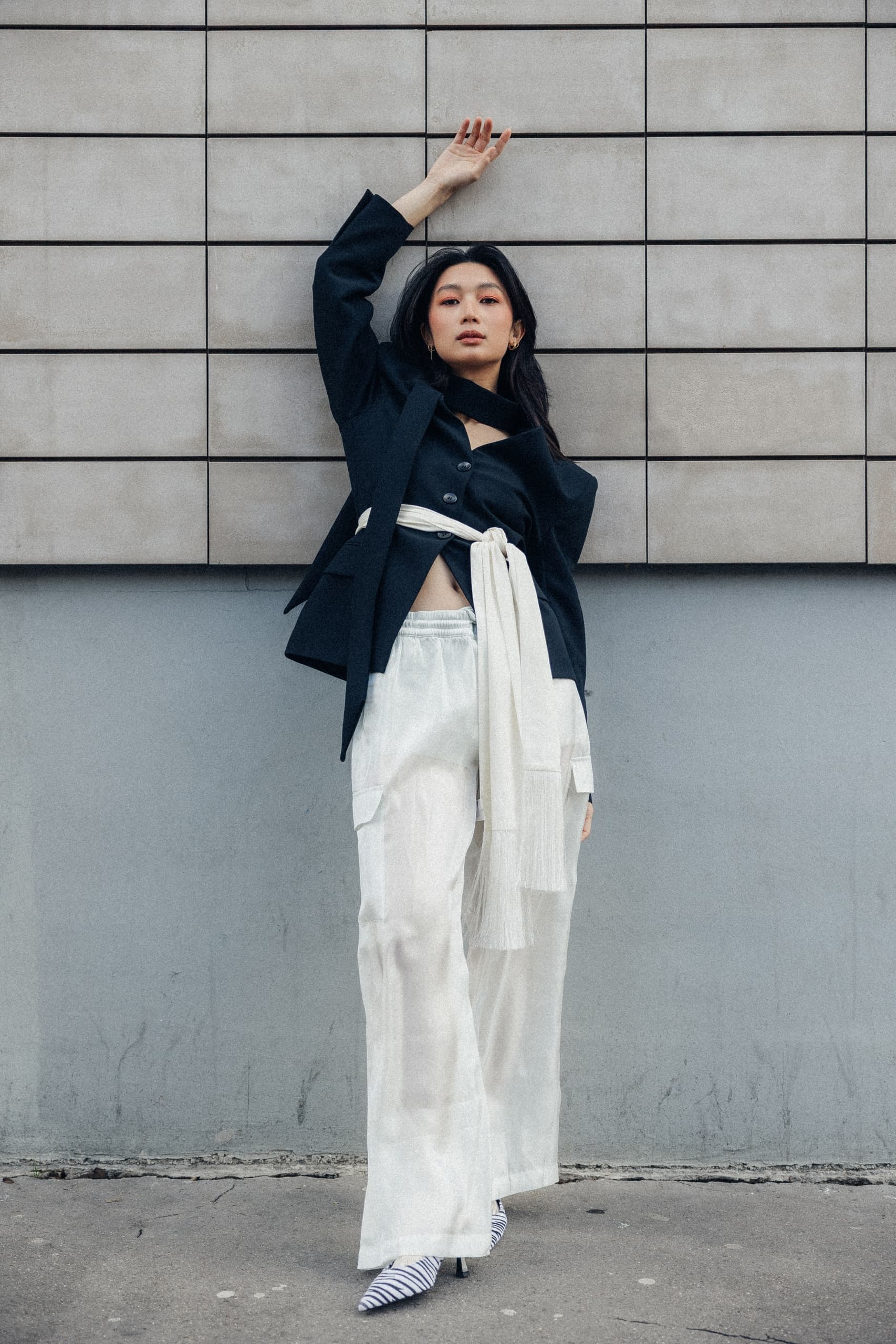 Fashionable woman posing in stylish black and white outfit against a modern wall.