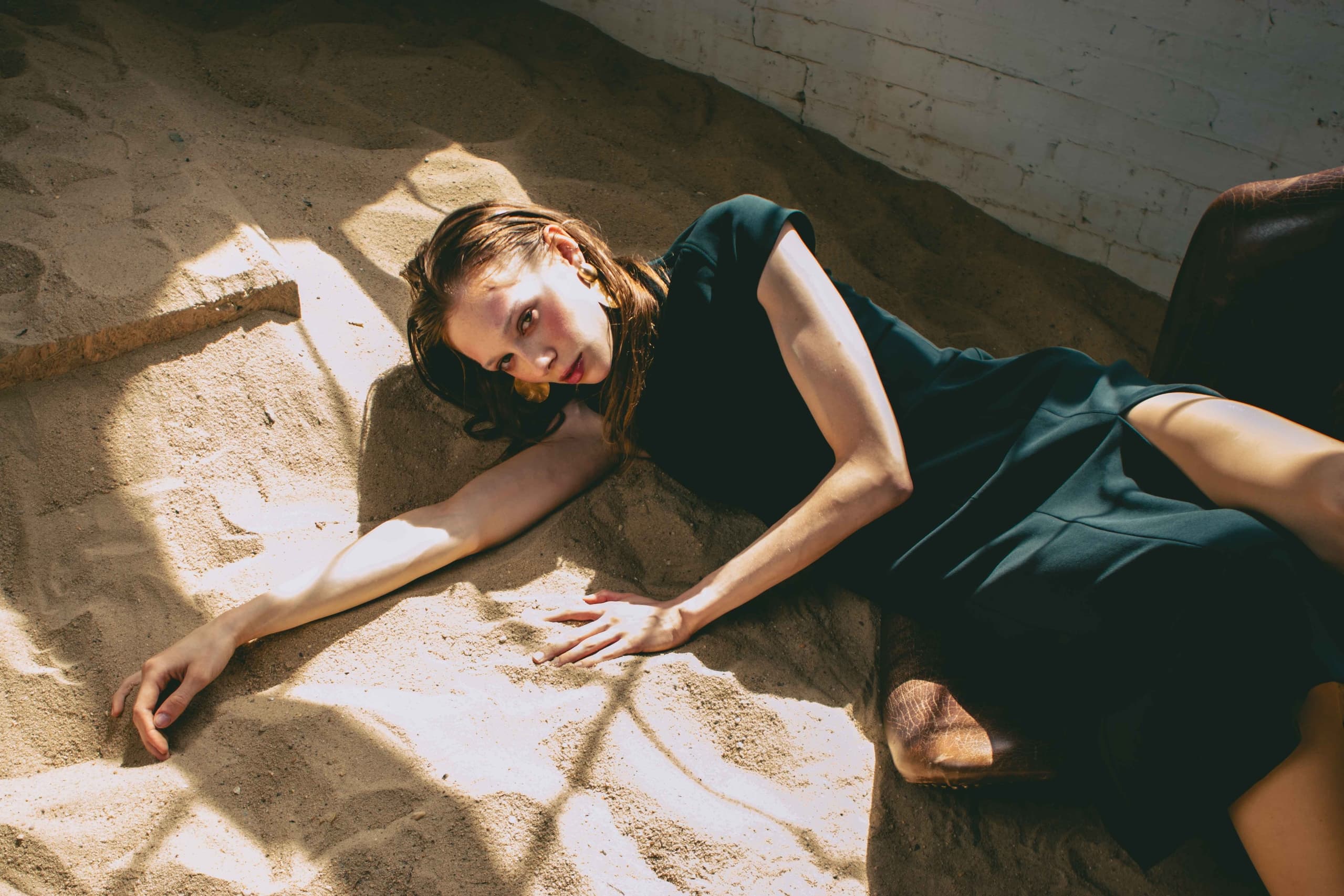 Woman in black dress lying on sand with dramatic lighting.