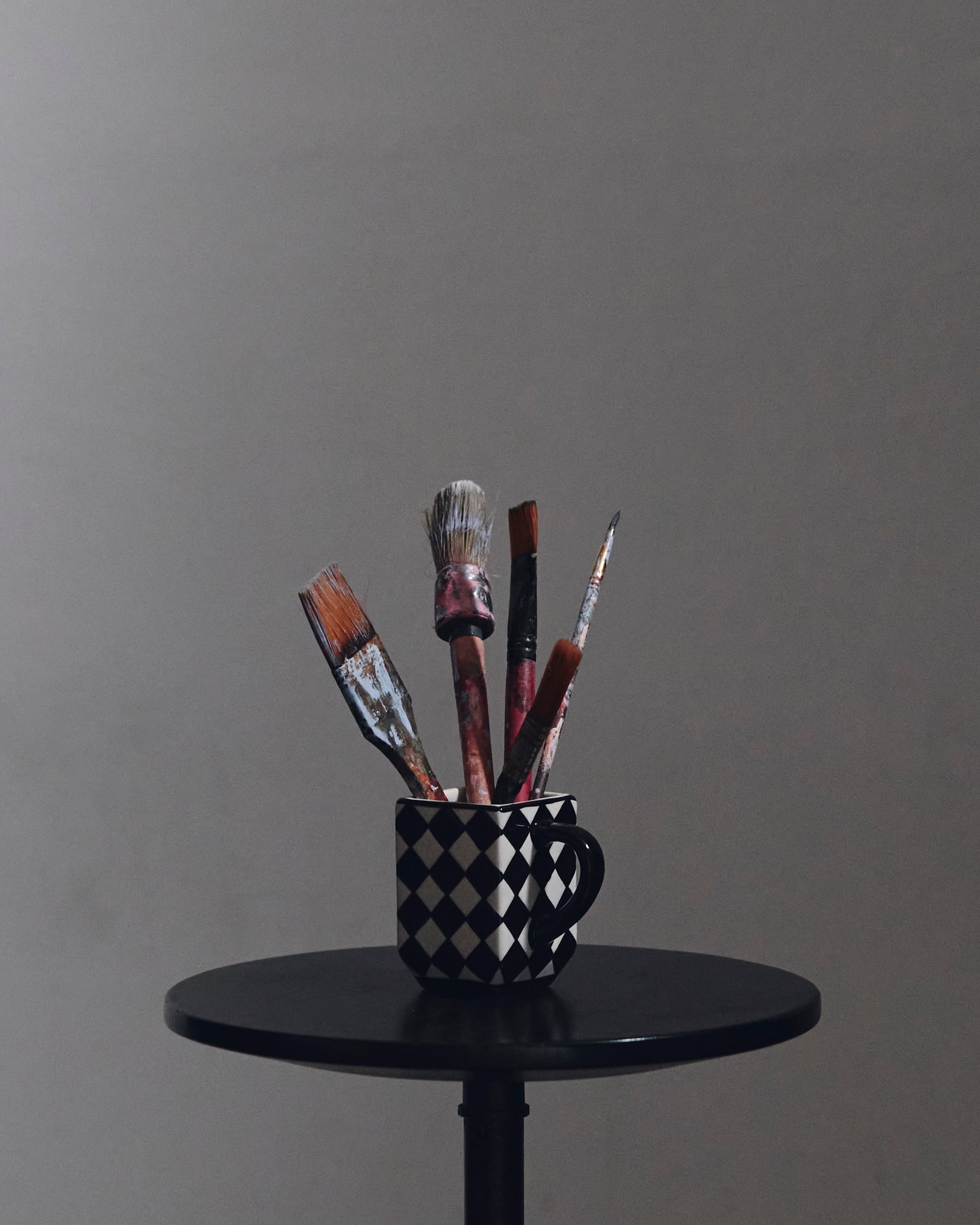 Paintbrushes in checkered mug on table against gray background.