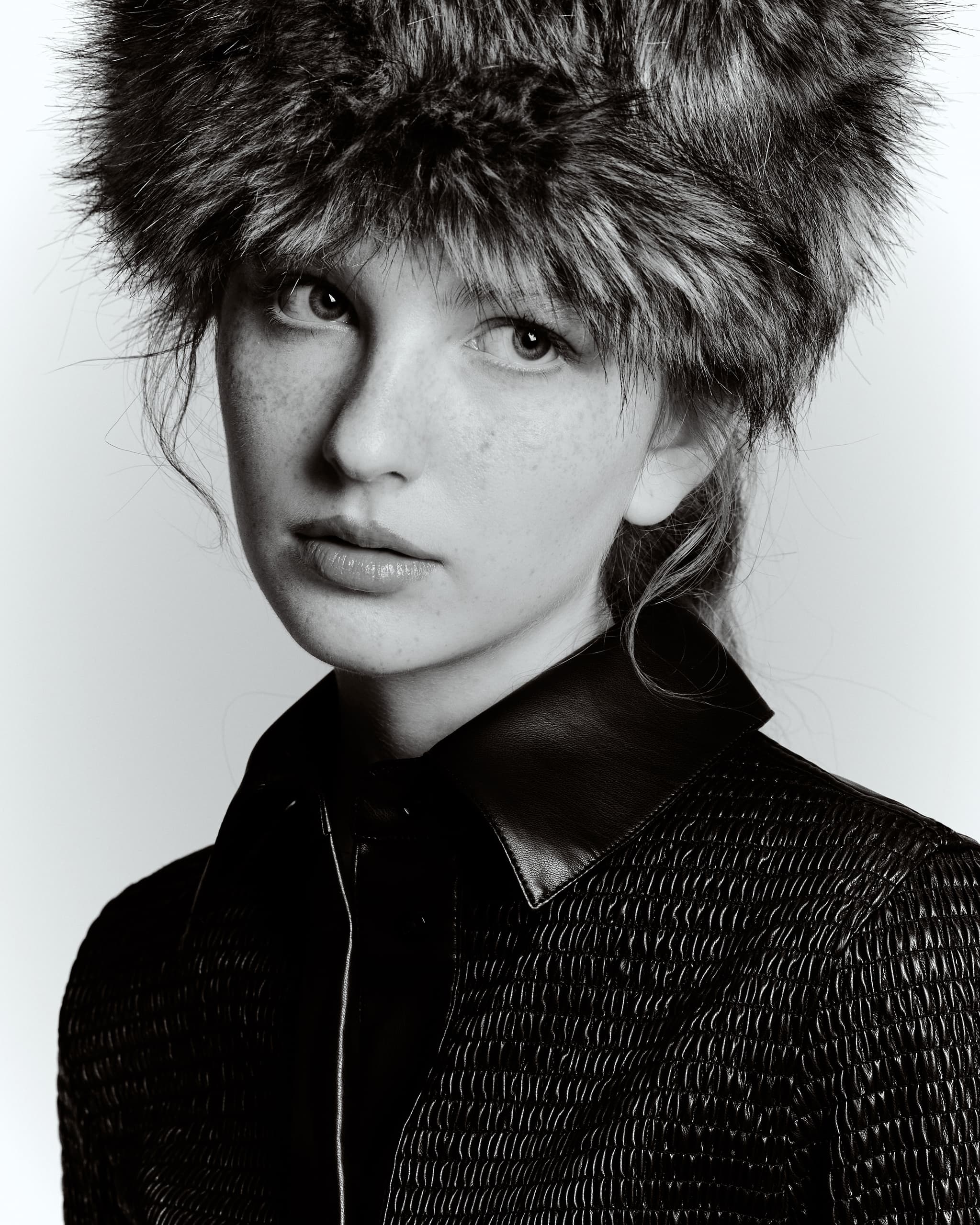 Monochrome portrait of a model in a fur hat and textured jacket.