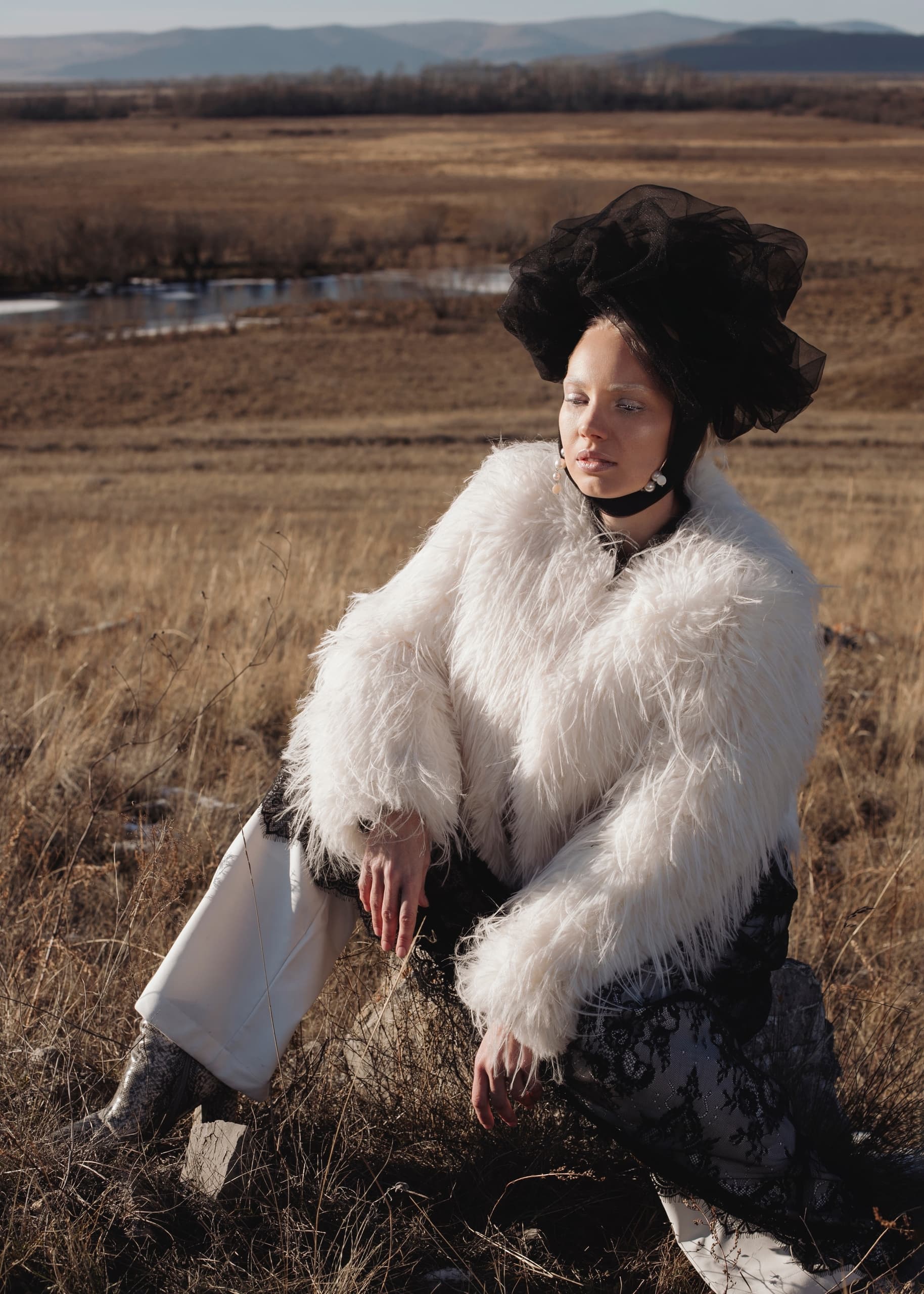 Fashionable woman in white fur coat in scenic grassland.