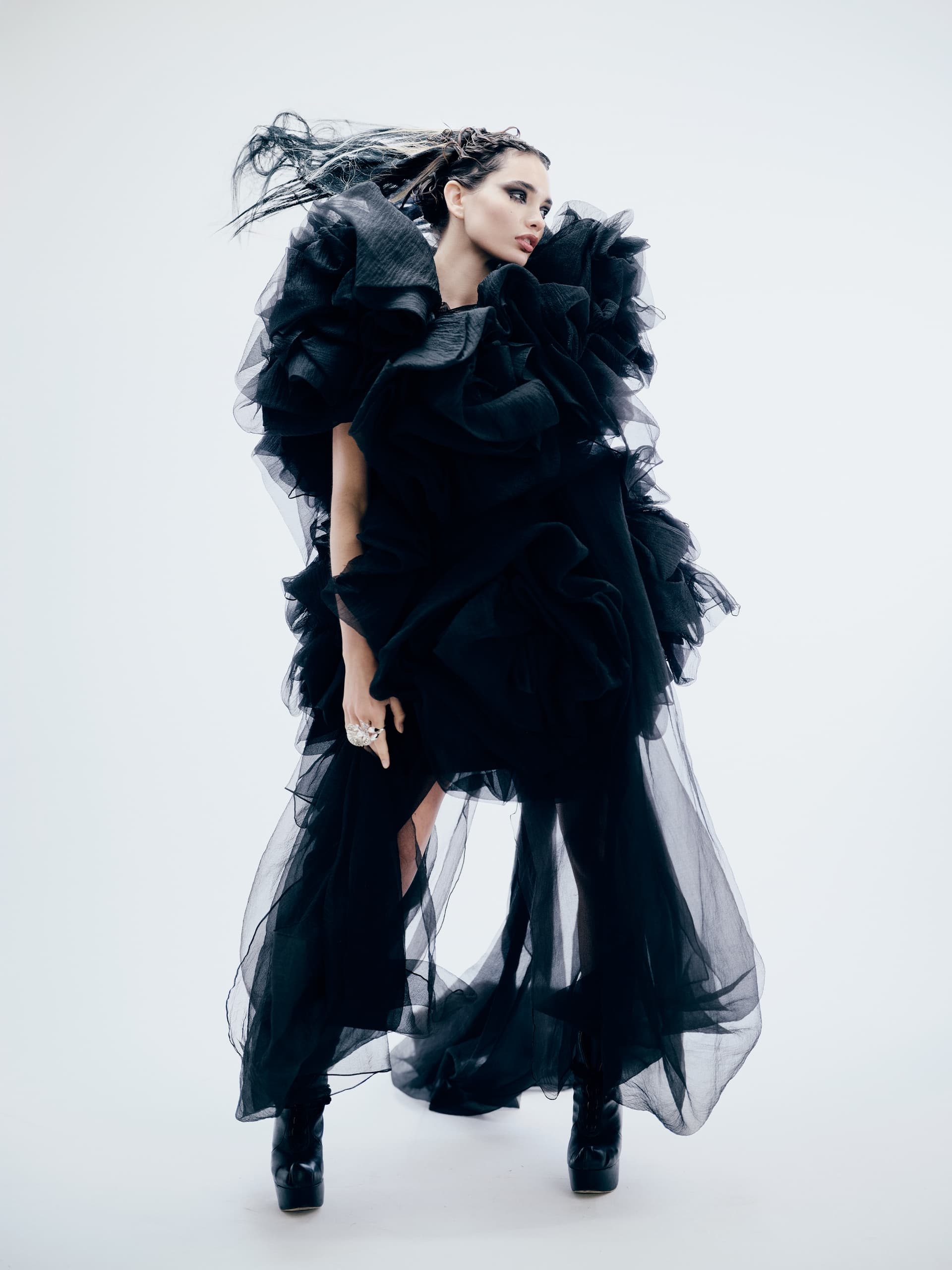 Fashion-forward model in avant-garde black gown with ruffled layers and dramatic pose.